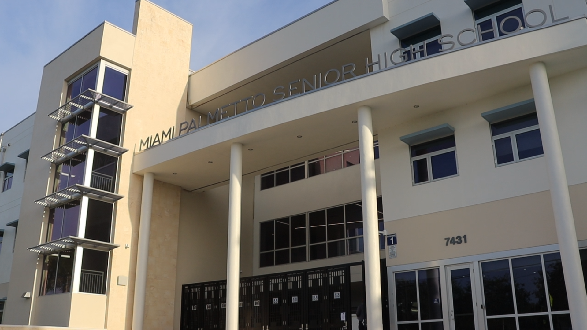 Front gate of a two-story school building with the school name in metal lettering above the entrance.