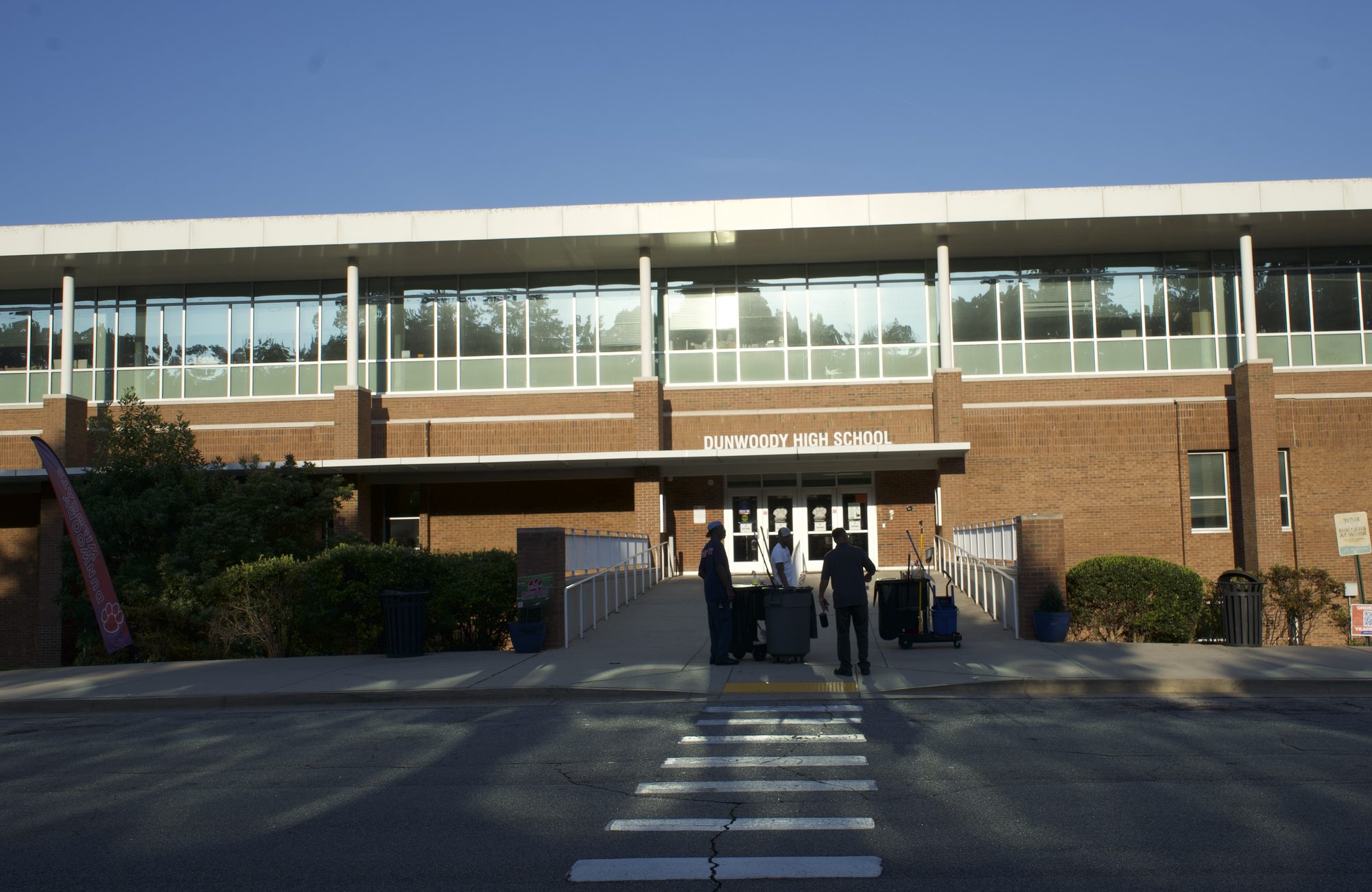 Two-story brick high school building exterior with people near the main entrance.