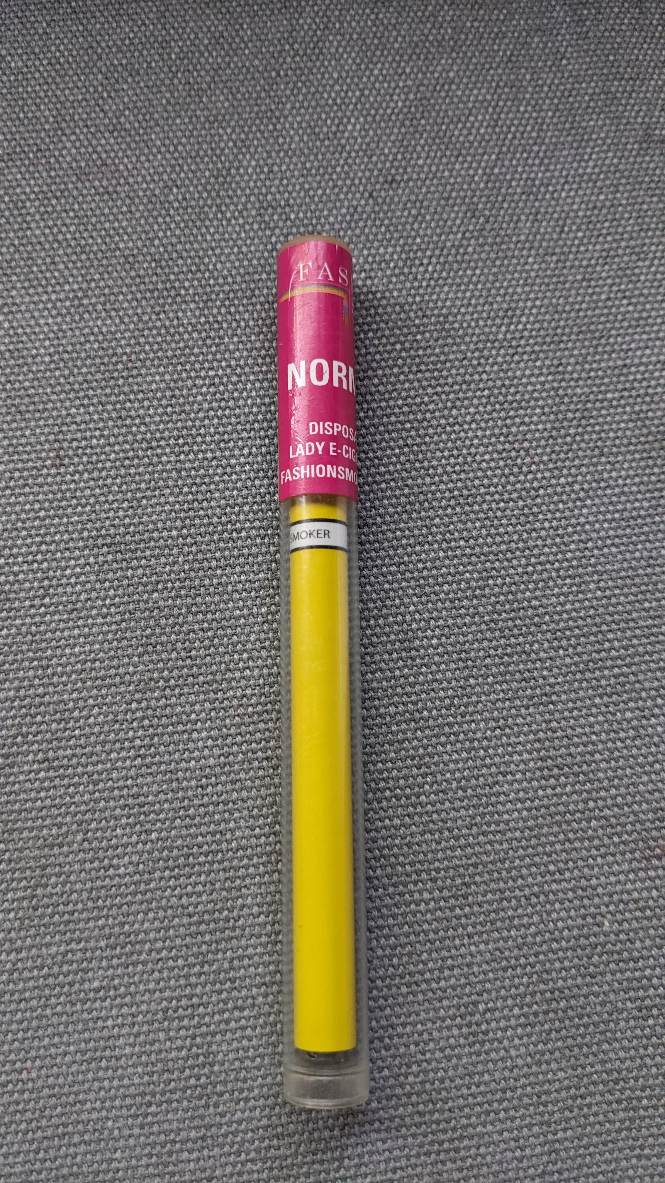 A slim yellow disposable vape pen with a pink label resting on gray fabric.