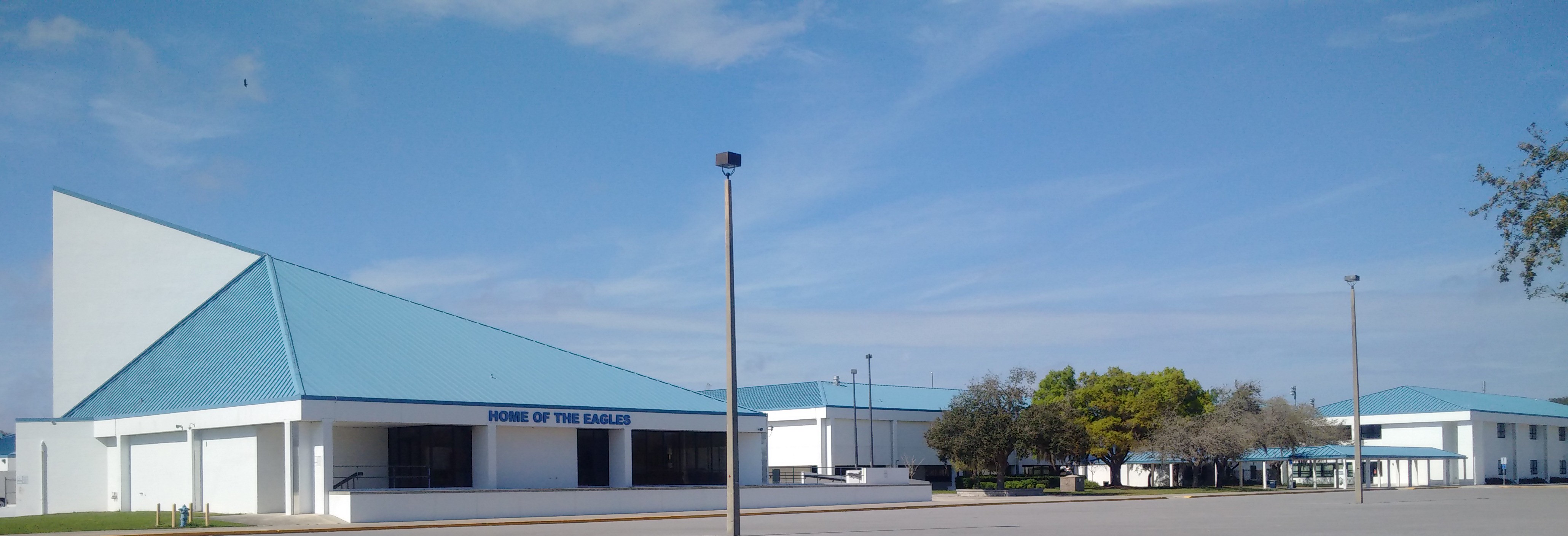 Single-story school building with teal roof and 'Home of the Eagles' sign under blue sky.