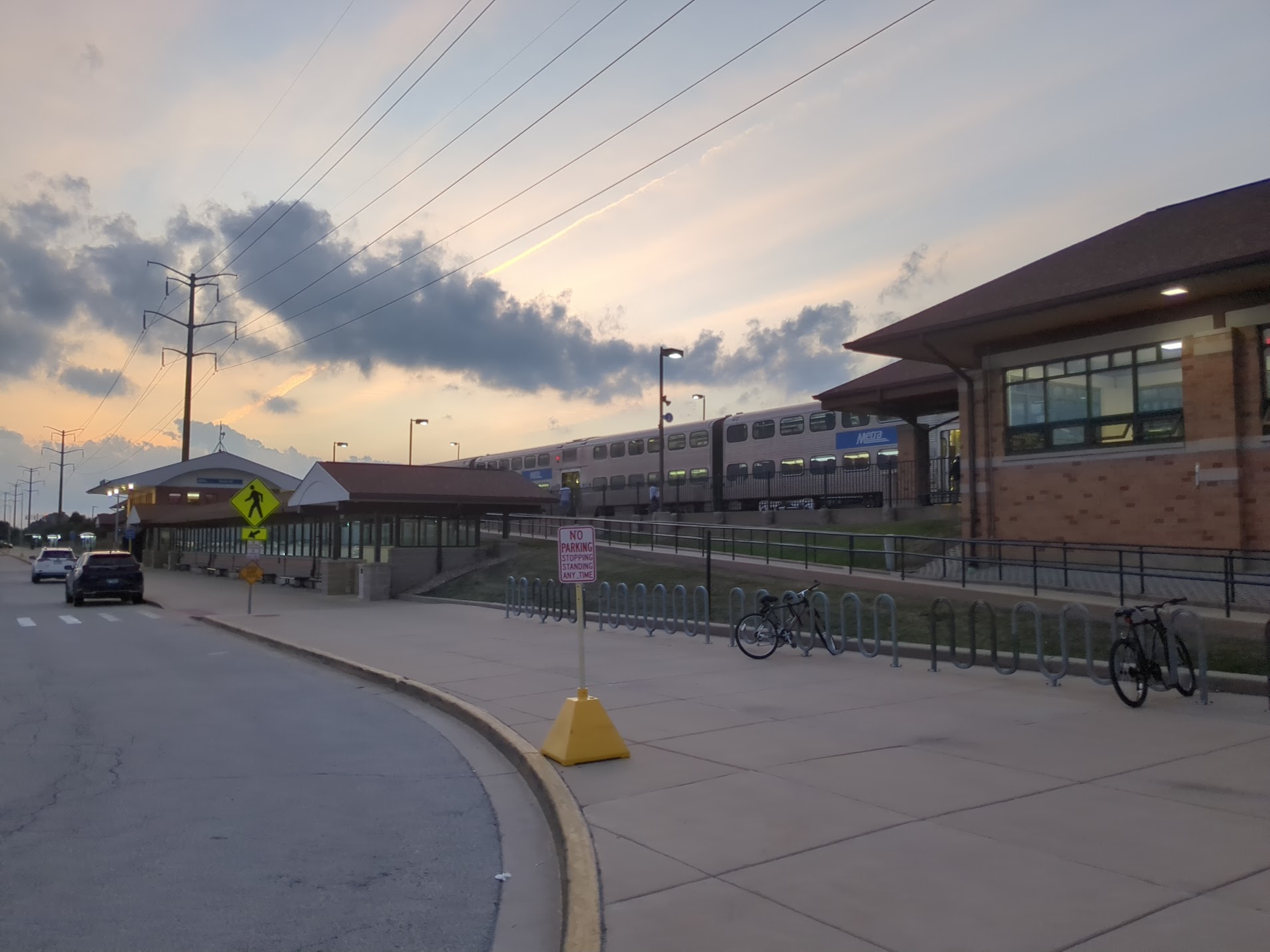 Metra train stopped at a commuter rail station with brick buildings and bike racks.