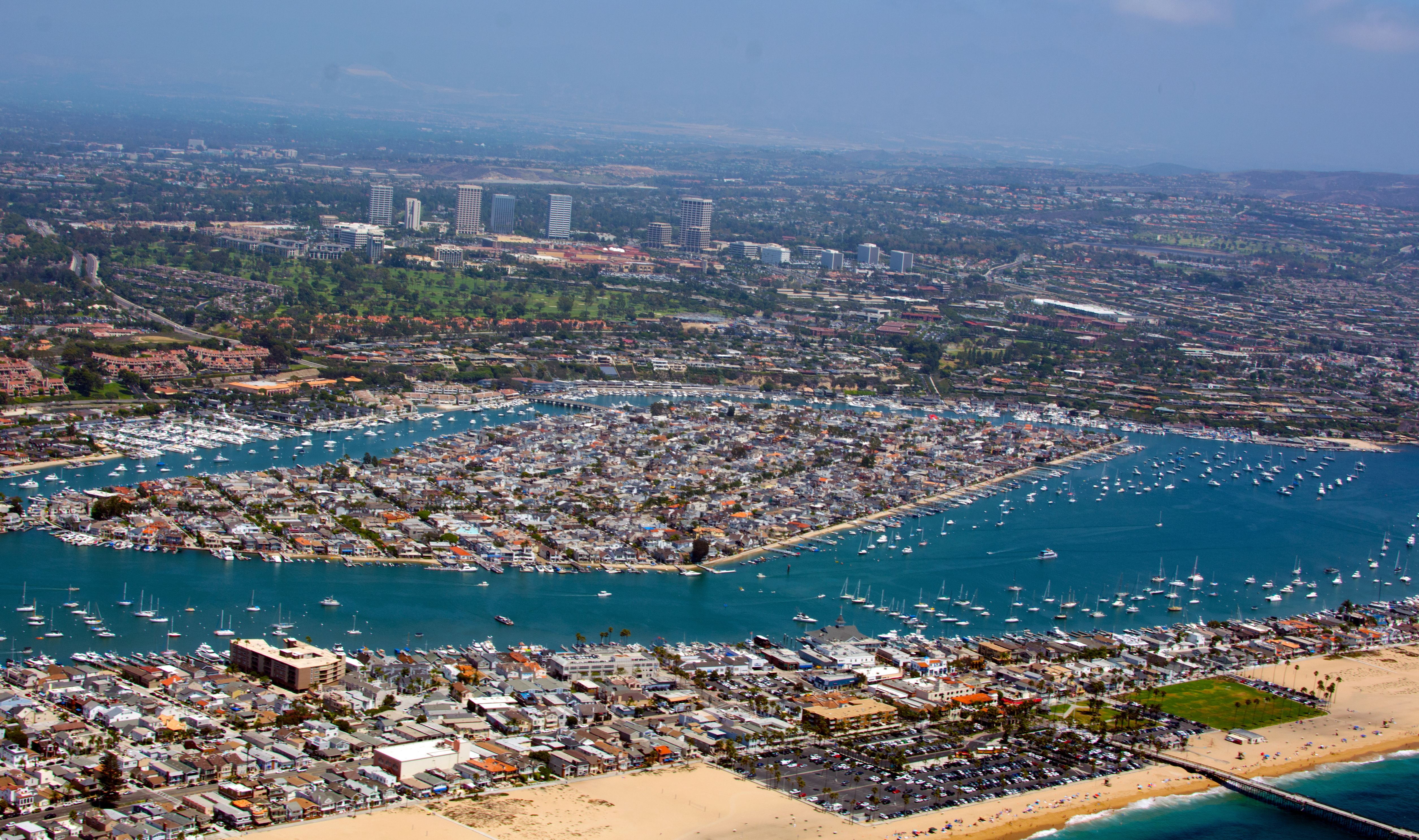 Aerial view of Balboa Island surrounded by harbor waters, sailboats, and dense residential homes.