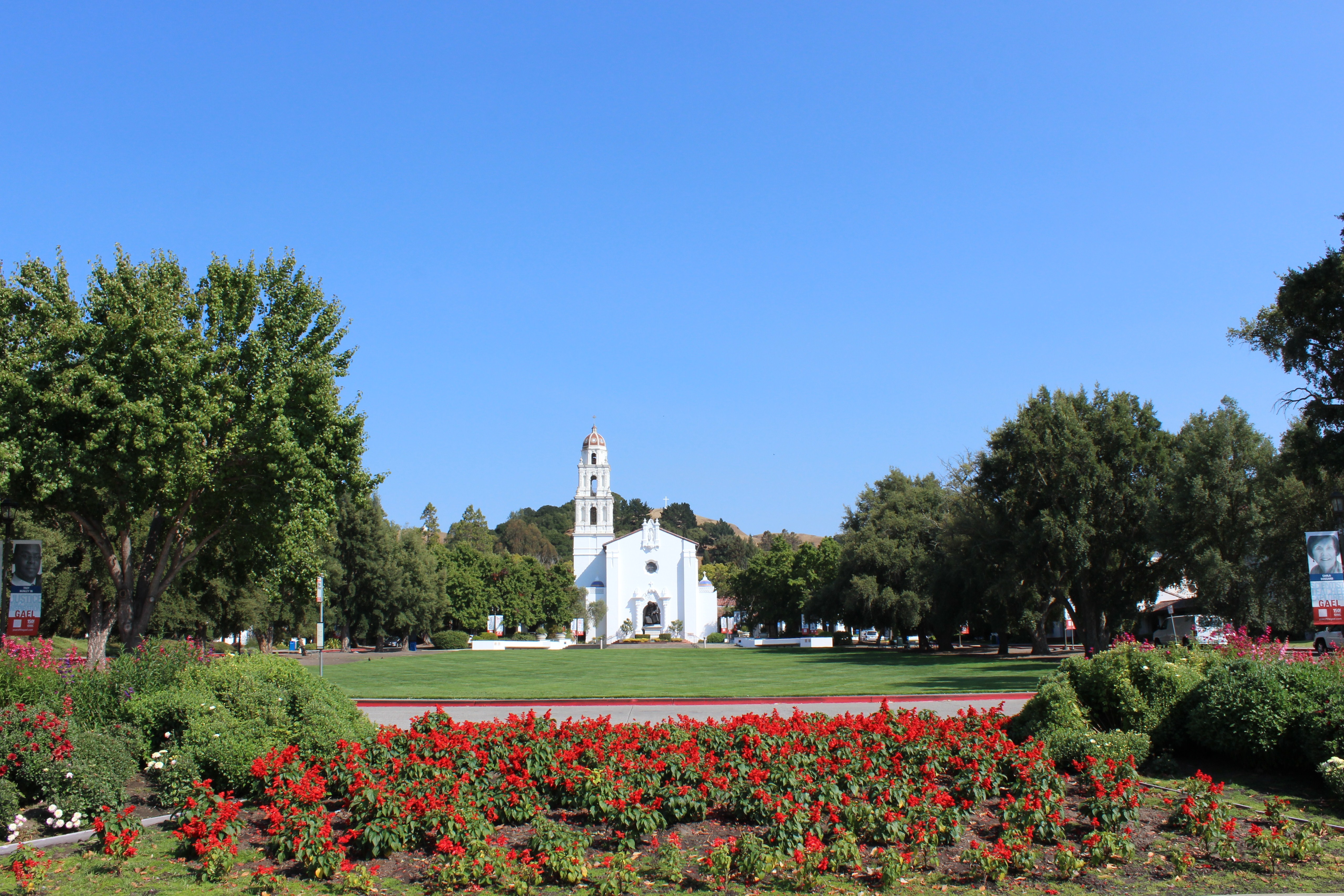 White Spanish mission-style chapel with bell tower on a green college campus.