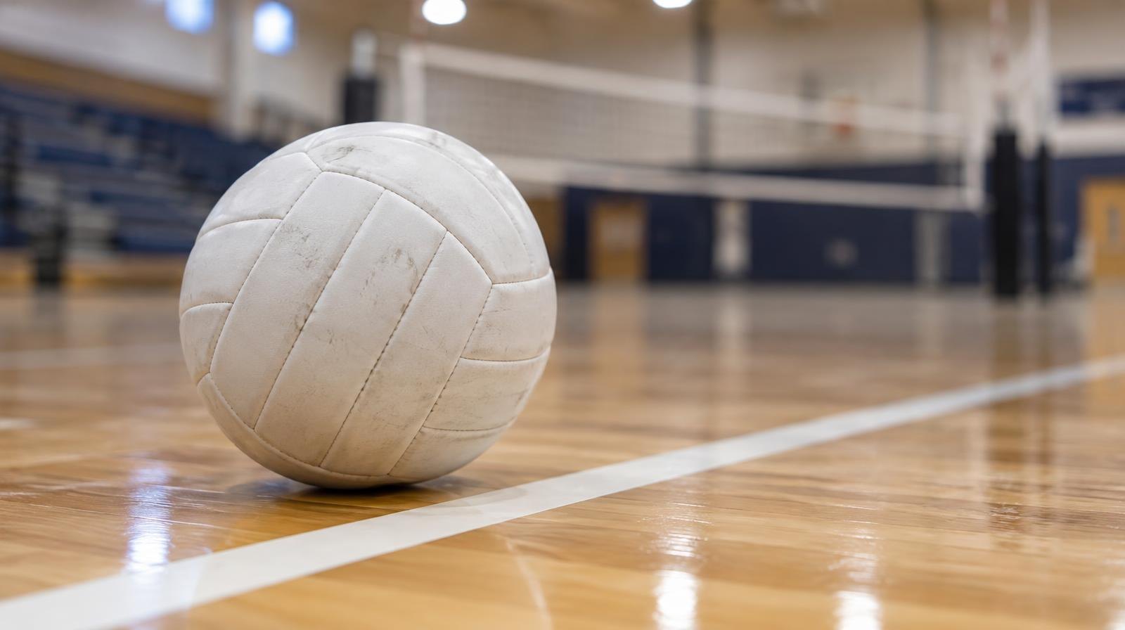 White volleyball resting on a hardwood gym floor near a painted boundary line.