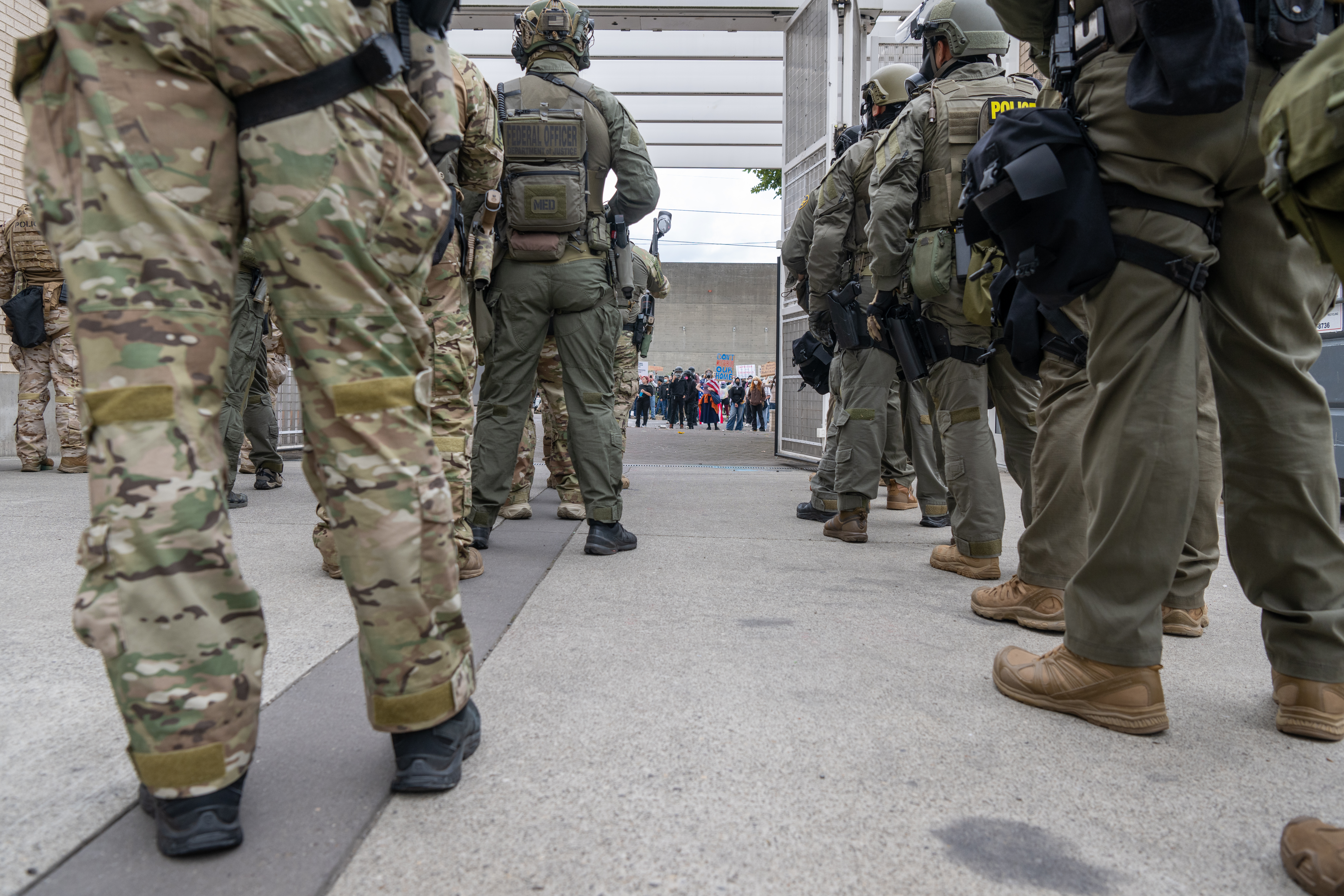 A row of federal officers in tactical gear and helmets stands on a city sidewalk.