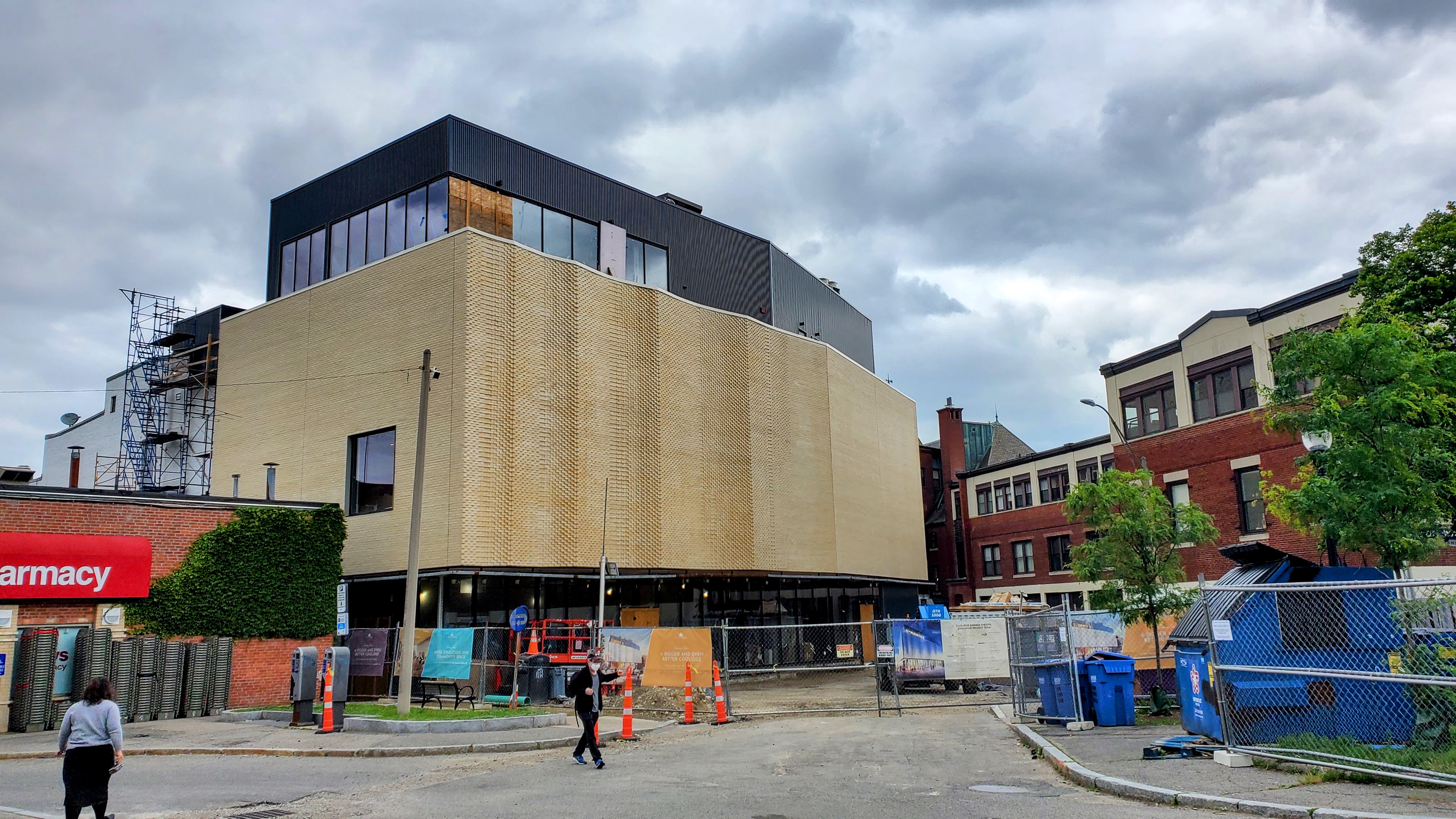 A building under construction with brick facade, construction fencing, and orange traffic cones on a Brookline street.