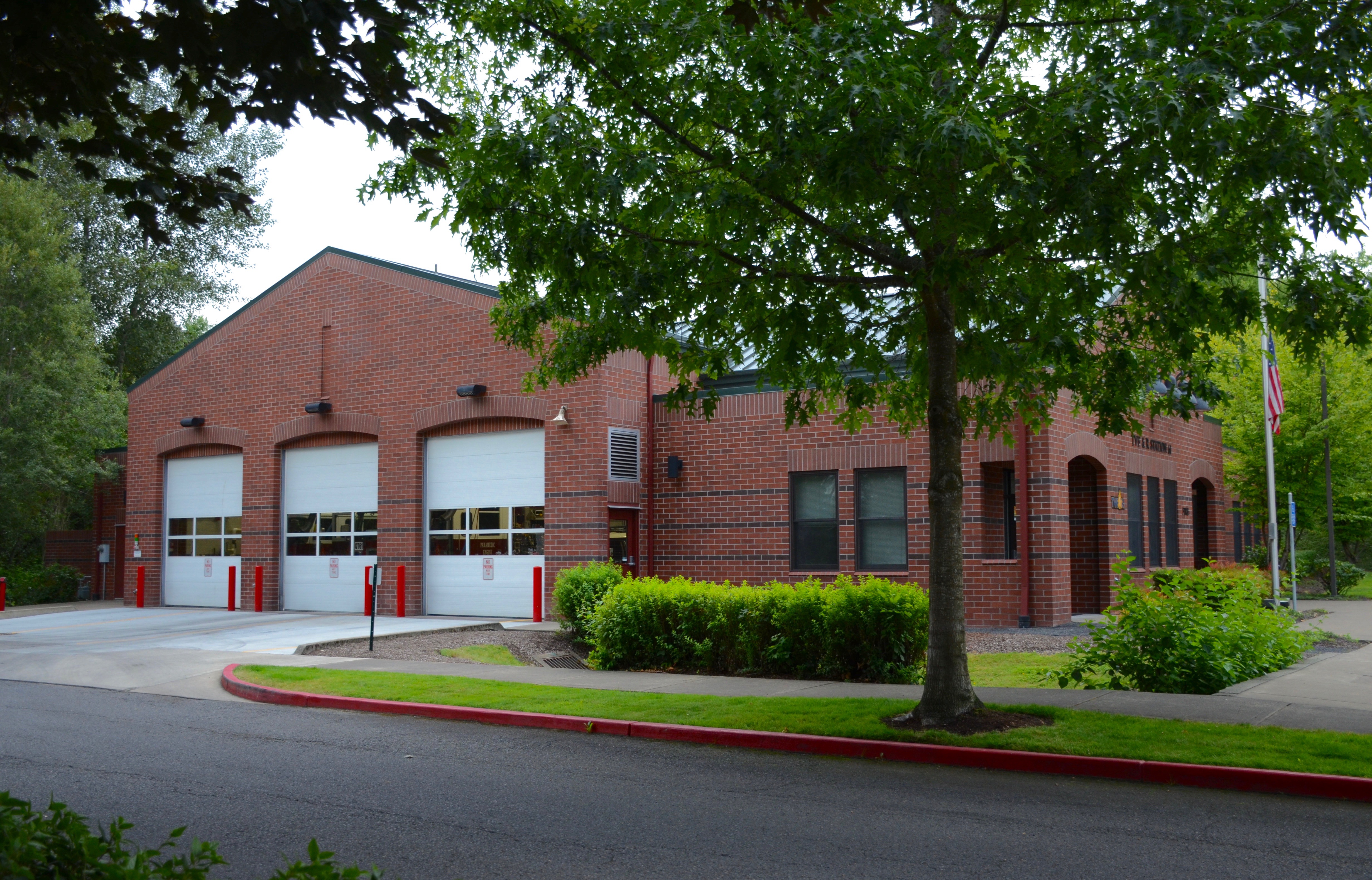 Red-brick fire station with white garage bay doors and a flagpole out front.