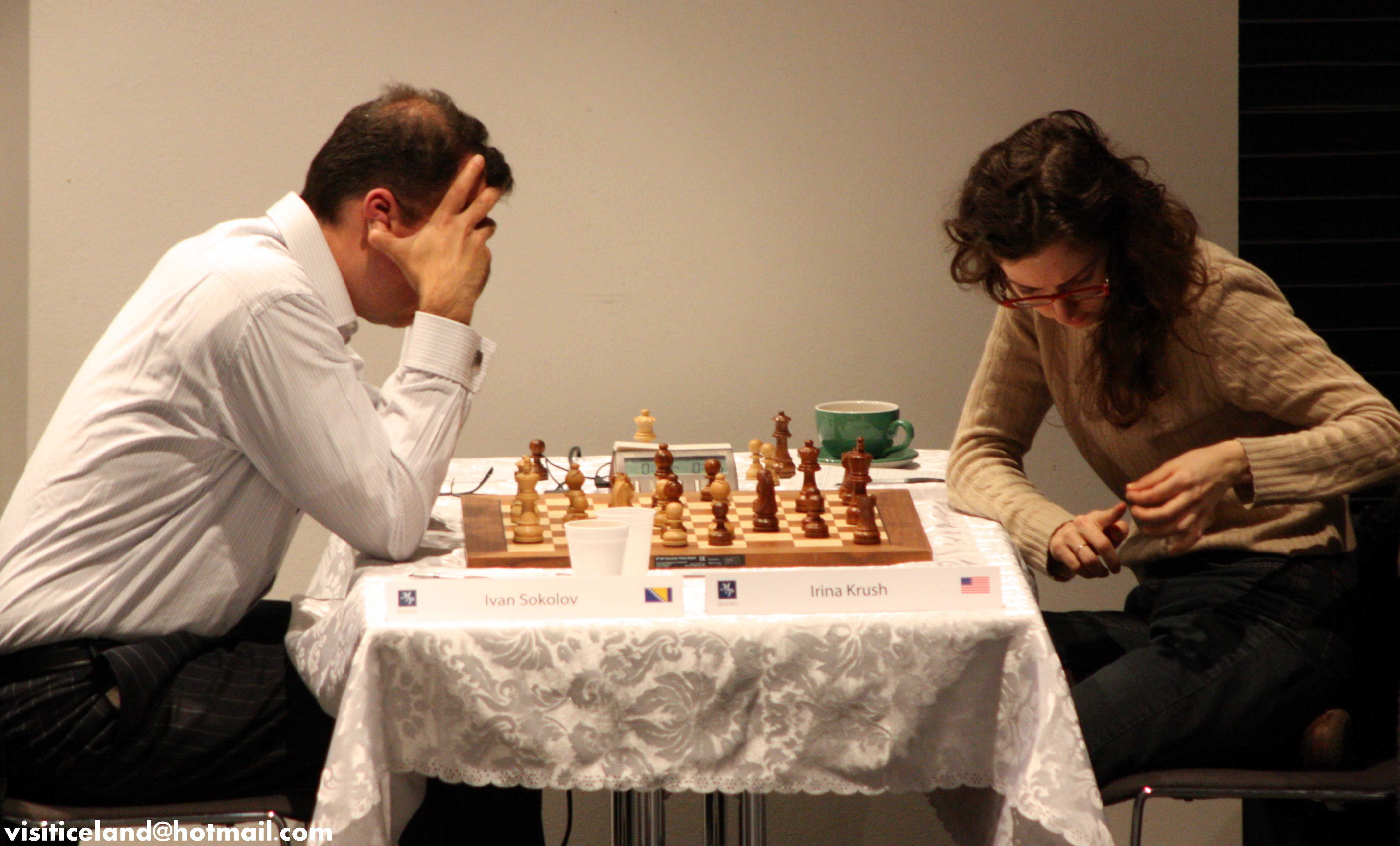 Two players seated at a chess board with pieces mid-game at a tournament.