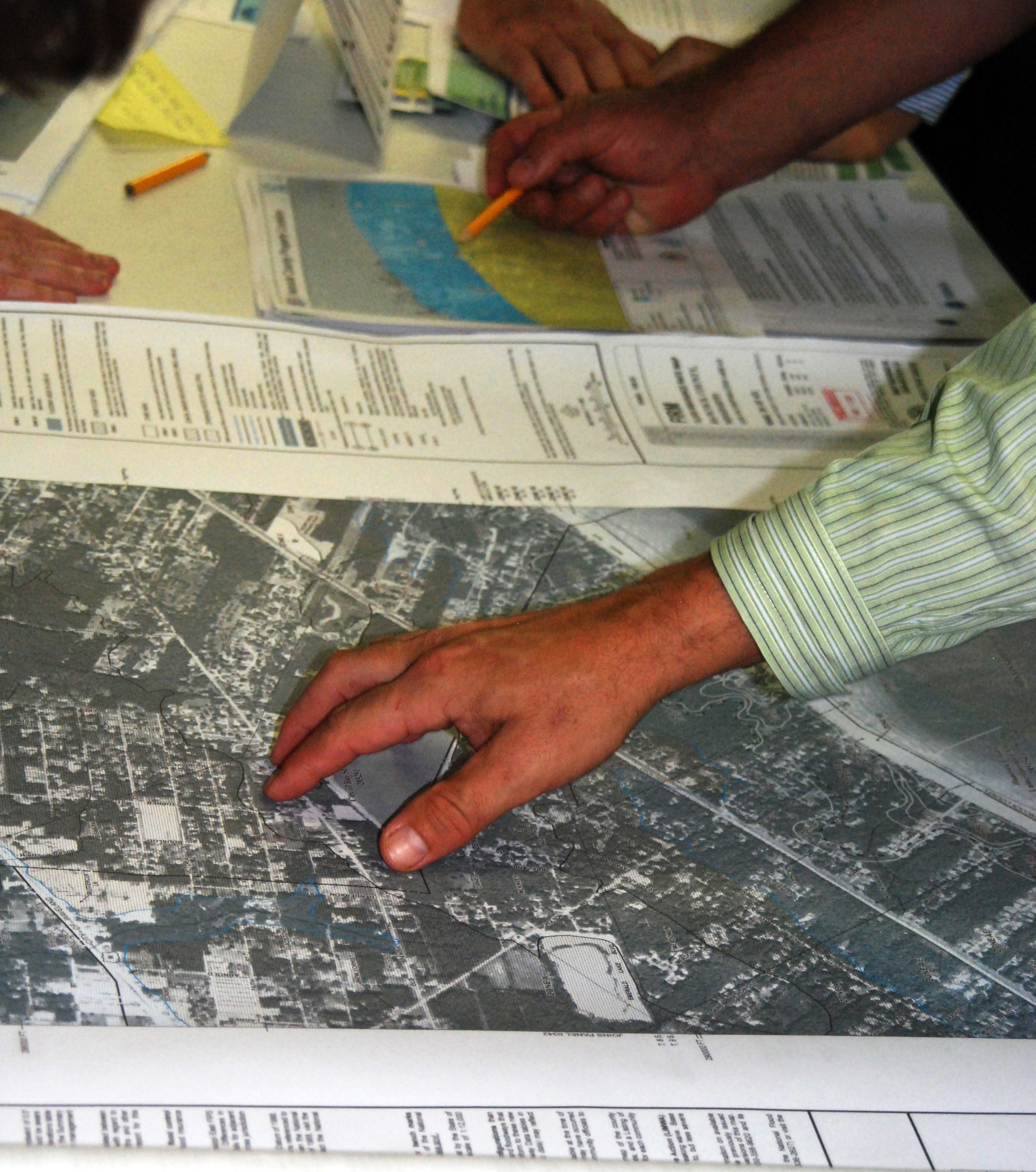 Several people lean over a table covered with large printed flood maps, pointing at zones.