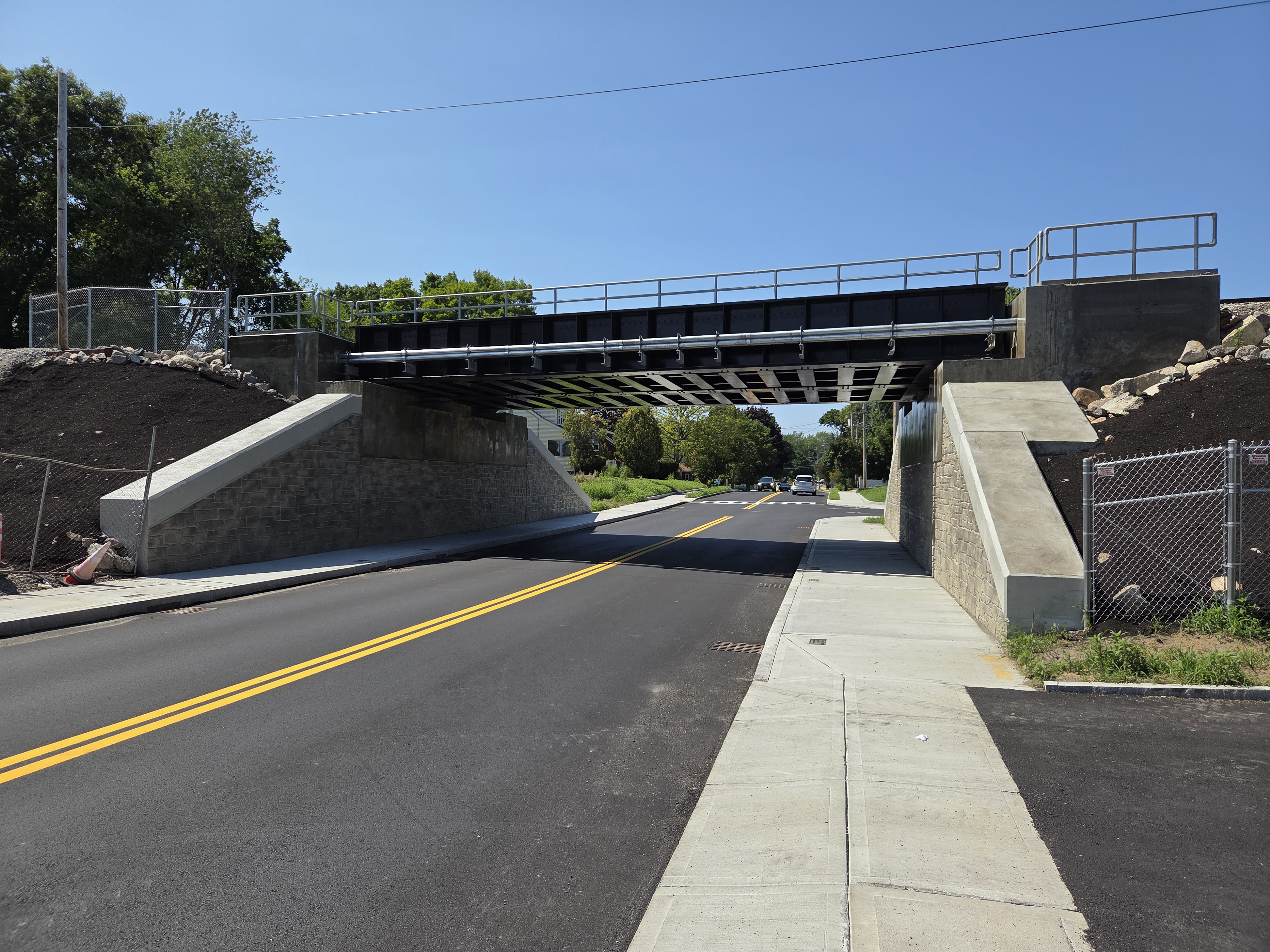Road passing under a newly rebuilt railroad bridge with fresh asphalt and concrete abutments.