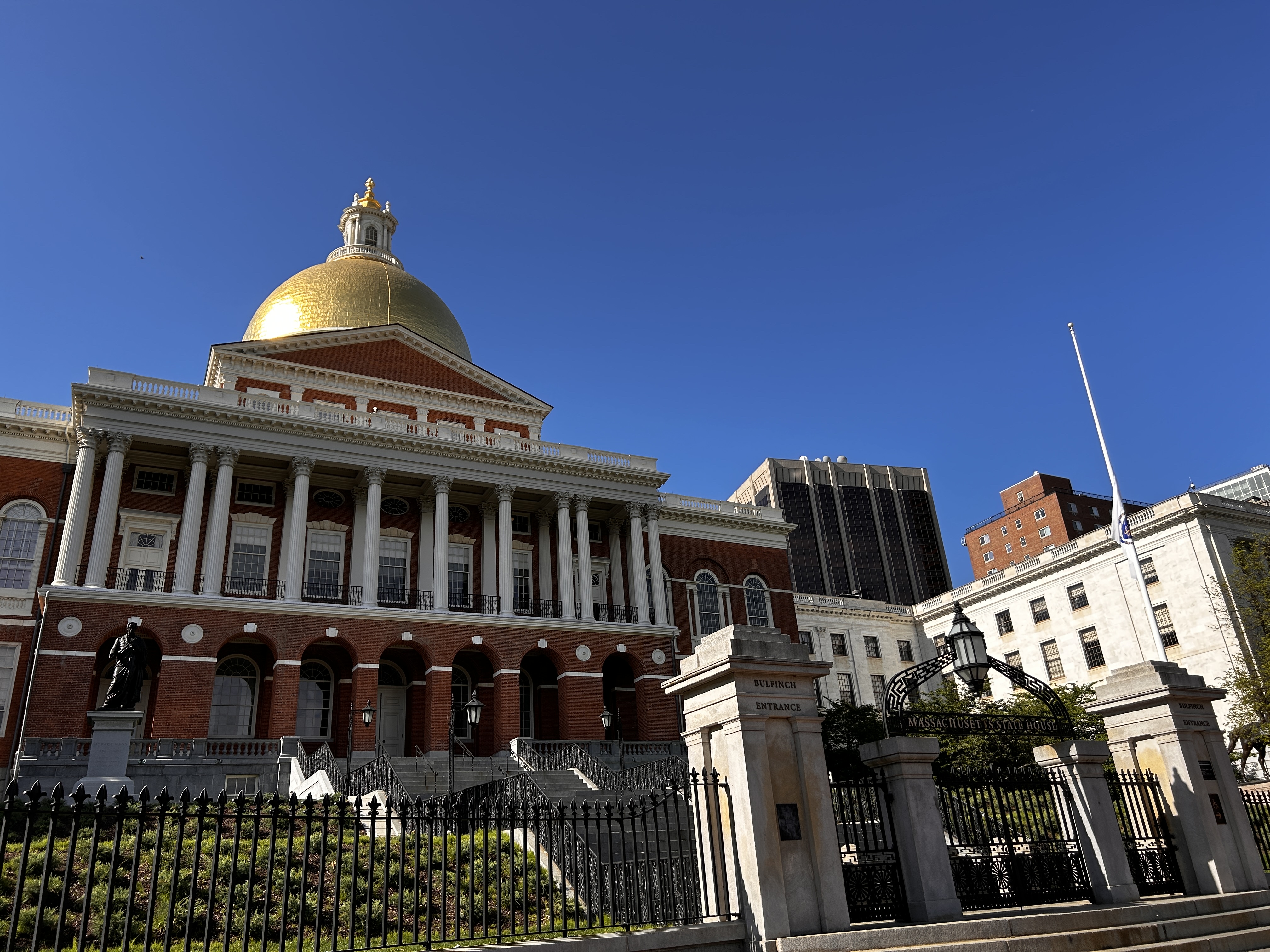 Gold-domed Massachusetts State House with red brick facade and iron fence.