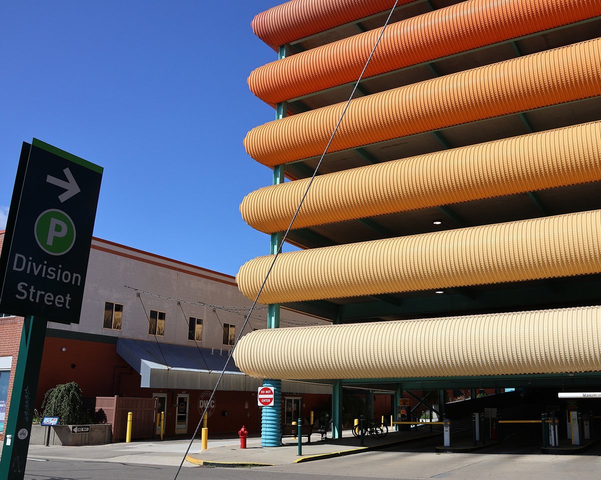 Multi-story parking garage with corrugated orange and tan facade panels and a green Division Street parking sign.