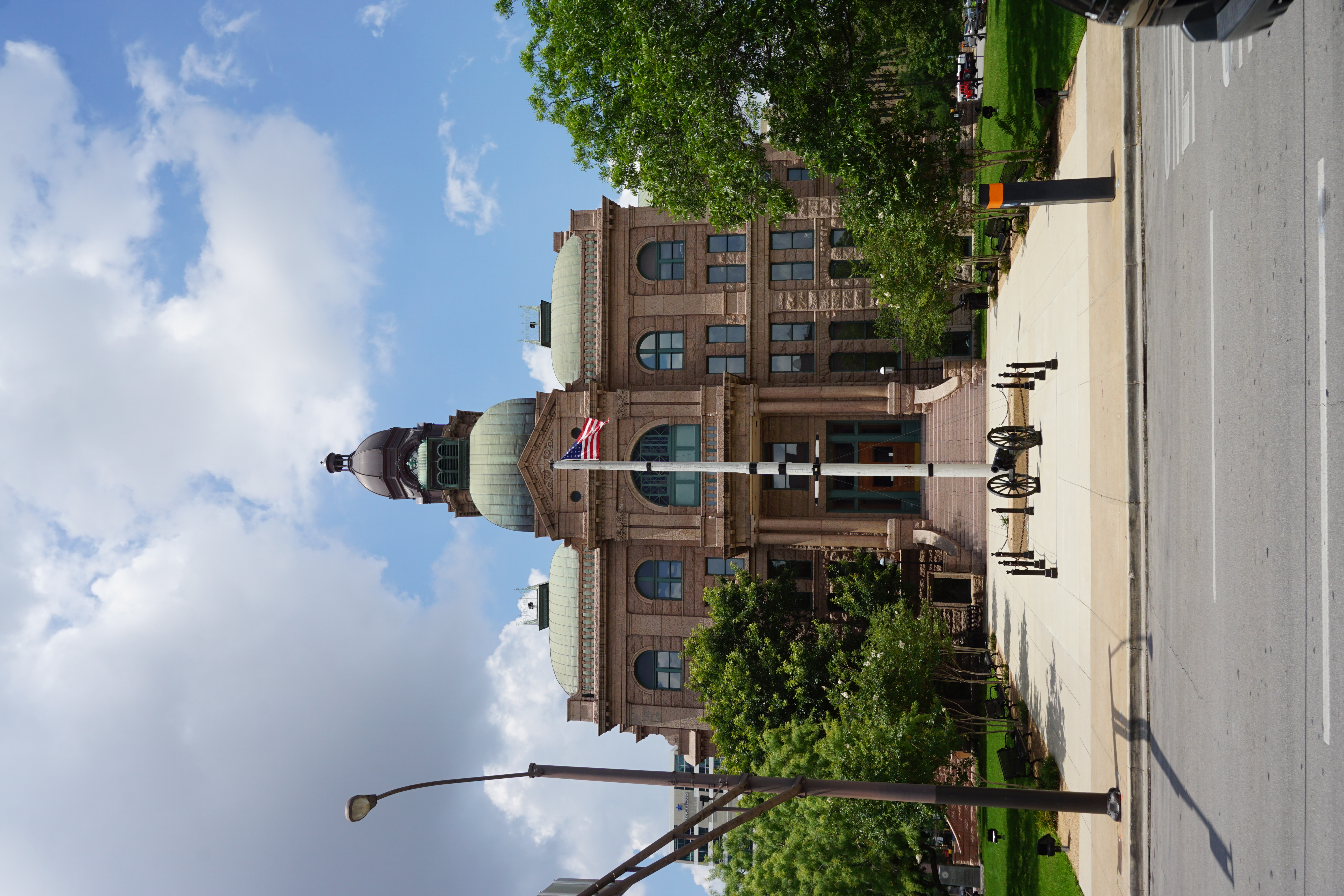 Courthouse with a green copper dome and American flag on a flagpole, under a partly cloudy sky.