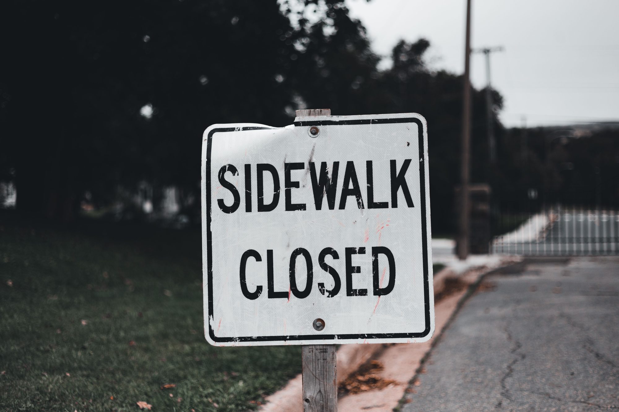 Close-up of a 'Sidewalk Closed' sign on a street, indicating obstruction.