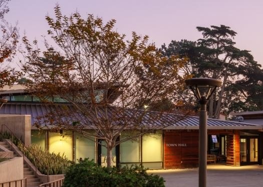 Low-rise town hall building with metal roof and wood-and-glass facade at dusk.
