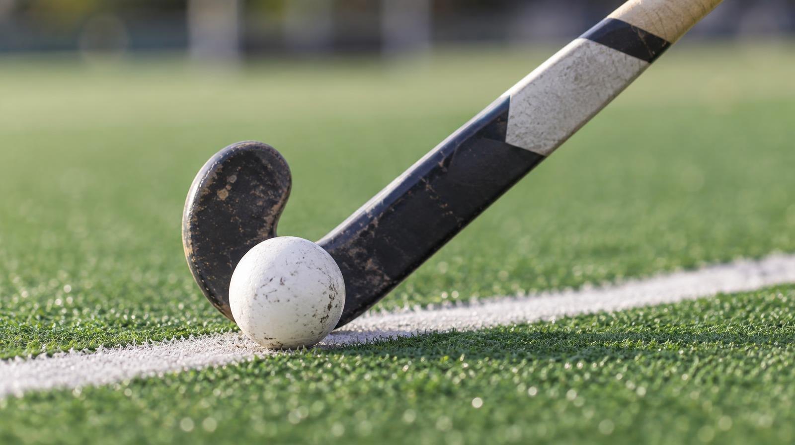 A field hockey stick and ball resting on green artificial turf near a white line.