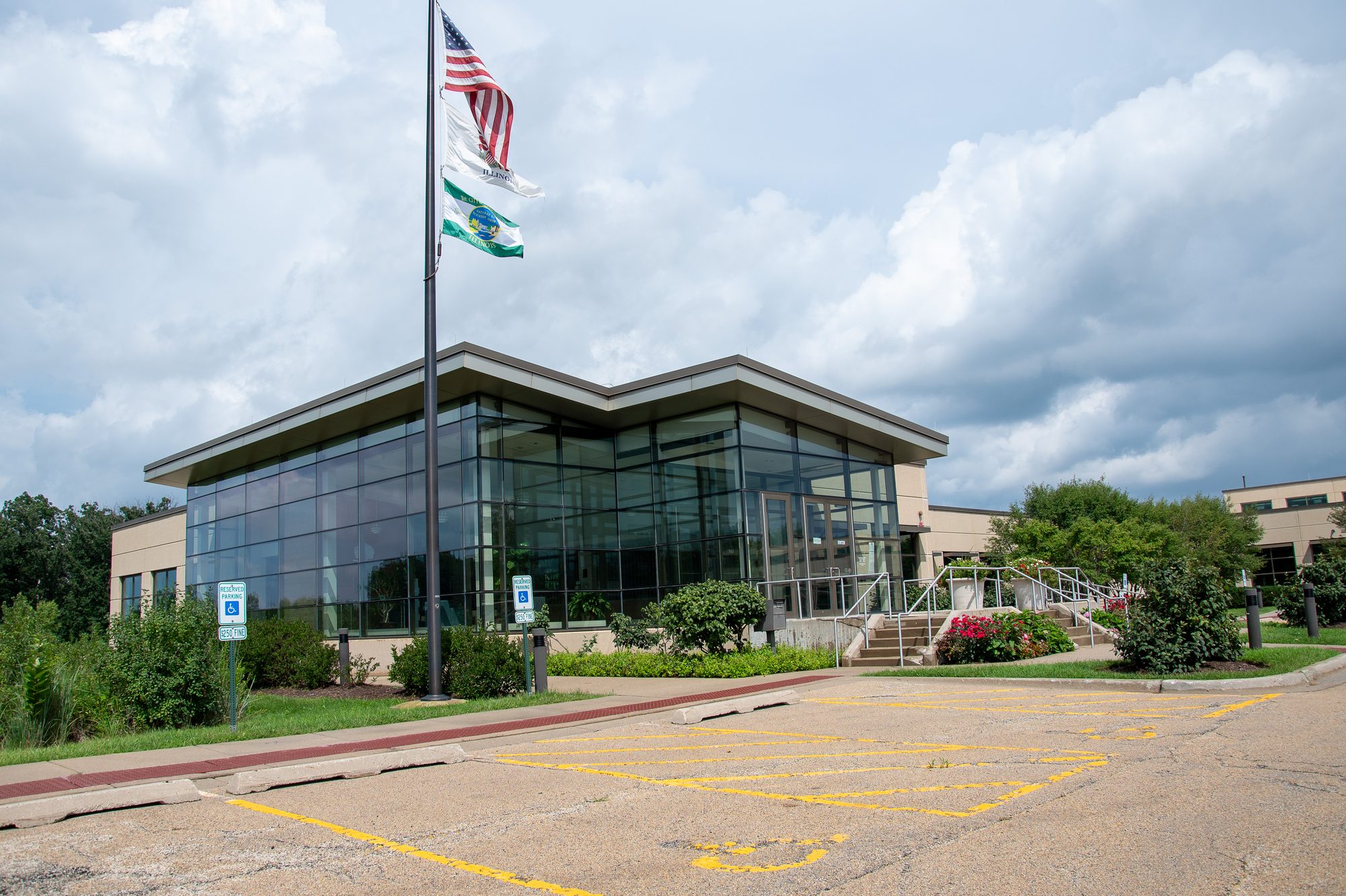 Modern glass-fronted municipal building with flags in a paved parking lot