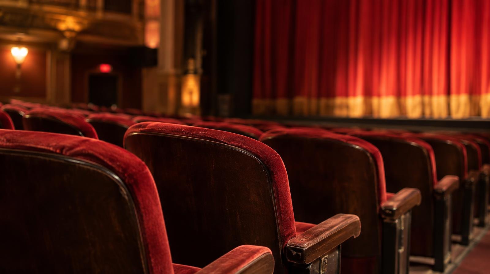 Rows of empty red velvet theater seats in a dimly lit auditorium.
