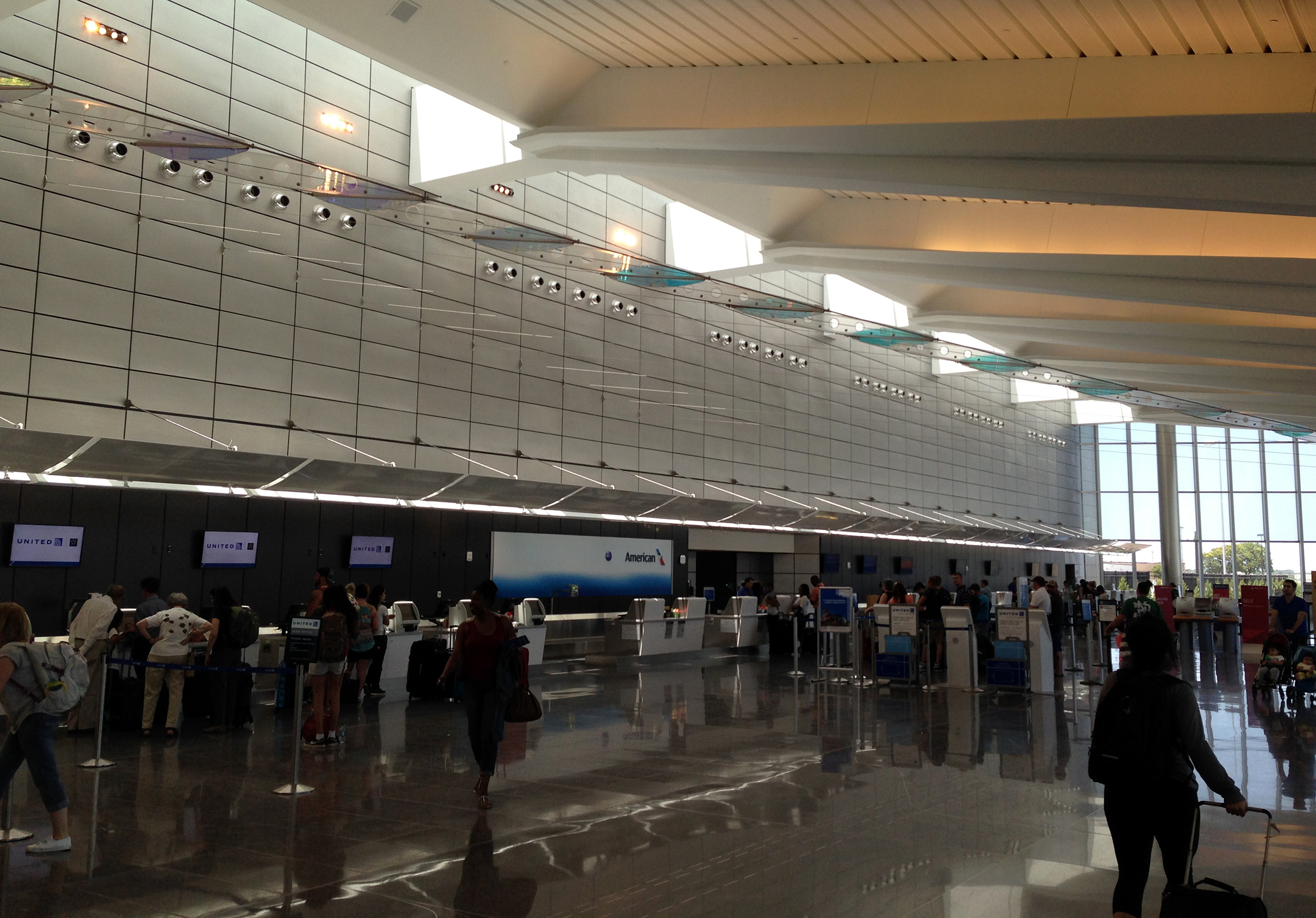 Airport check-in hall with airline counters, passengers, and angled ceiling windows.