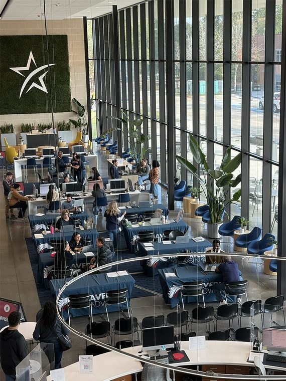 Overhead view of a college student center with students seated at blue tables near large windows.