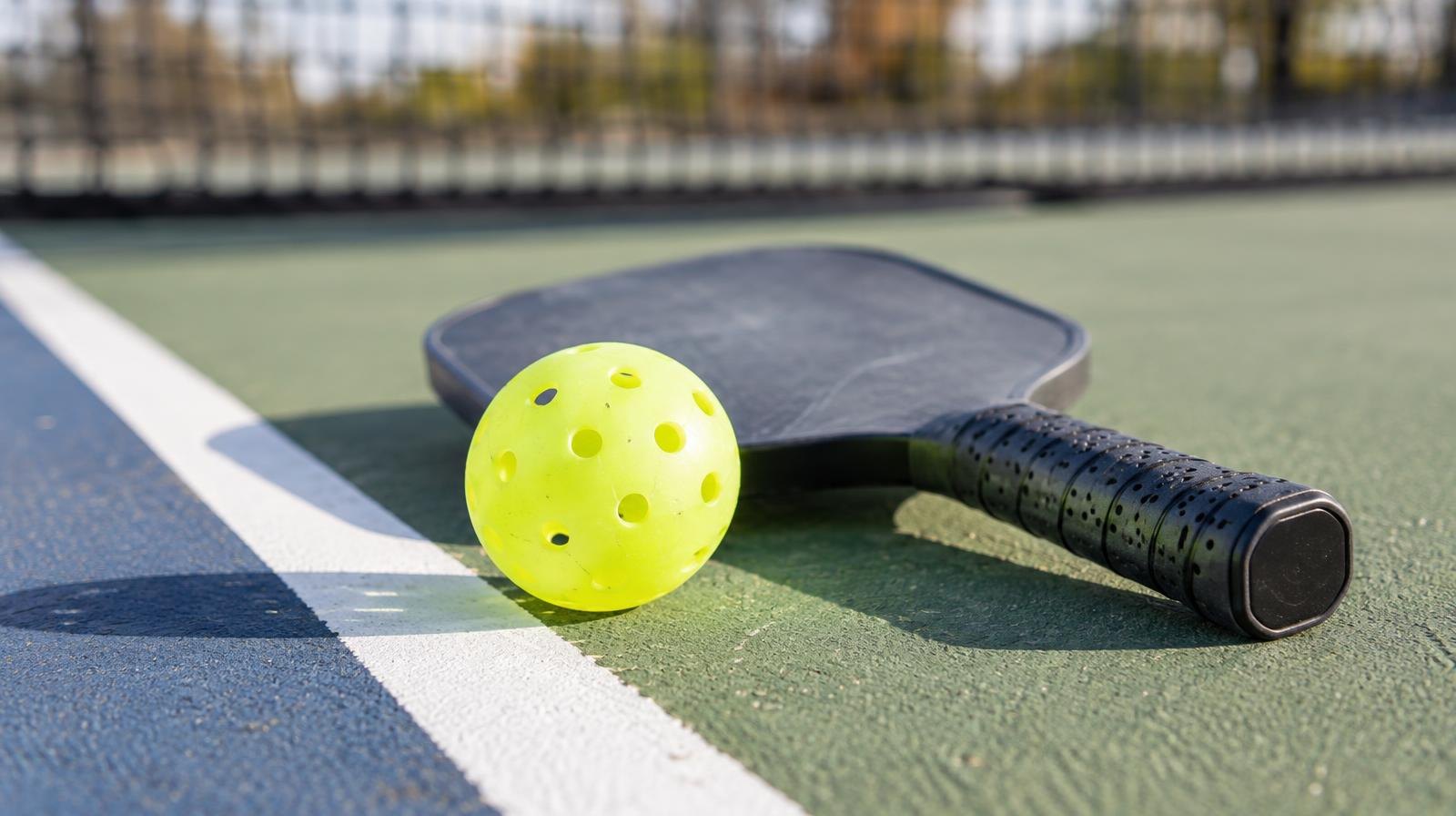 Pickleball paddle and yellow ball resting on a painted court surface.