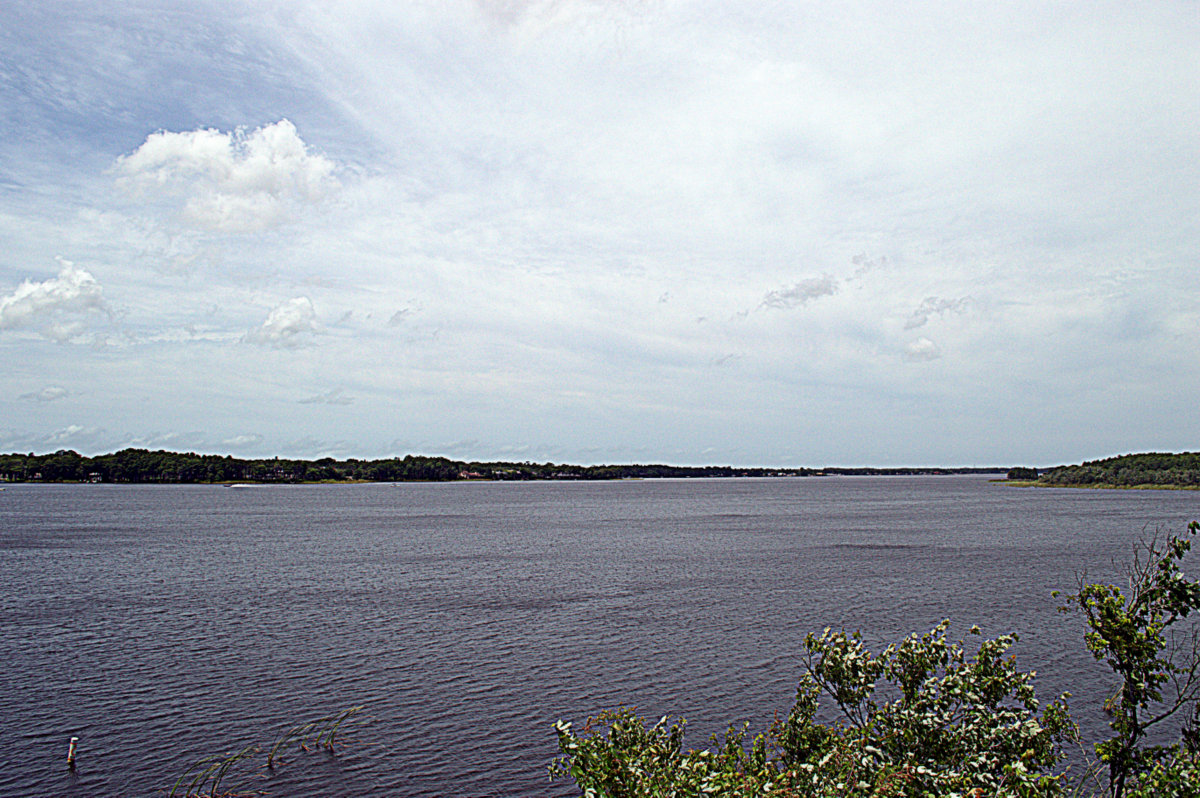 Wide view of a calm lake with tree-lined shores under a partly cloudy sky.