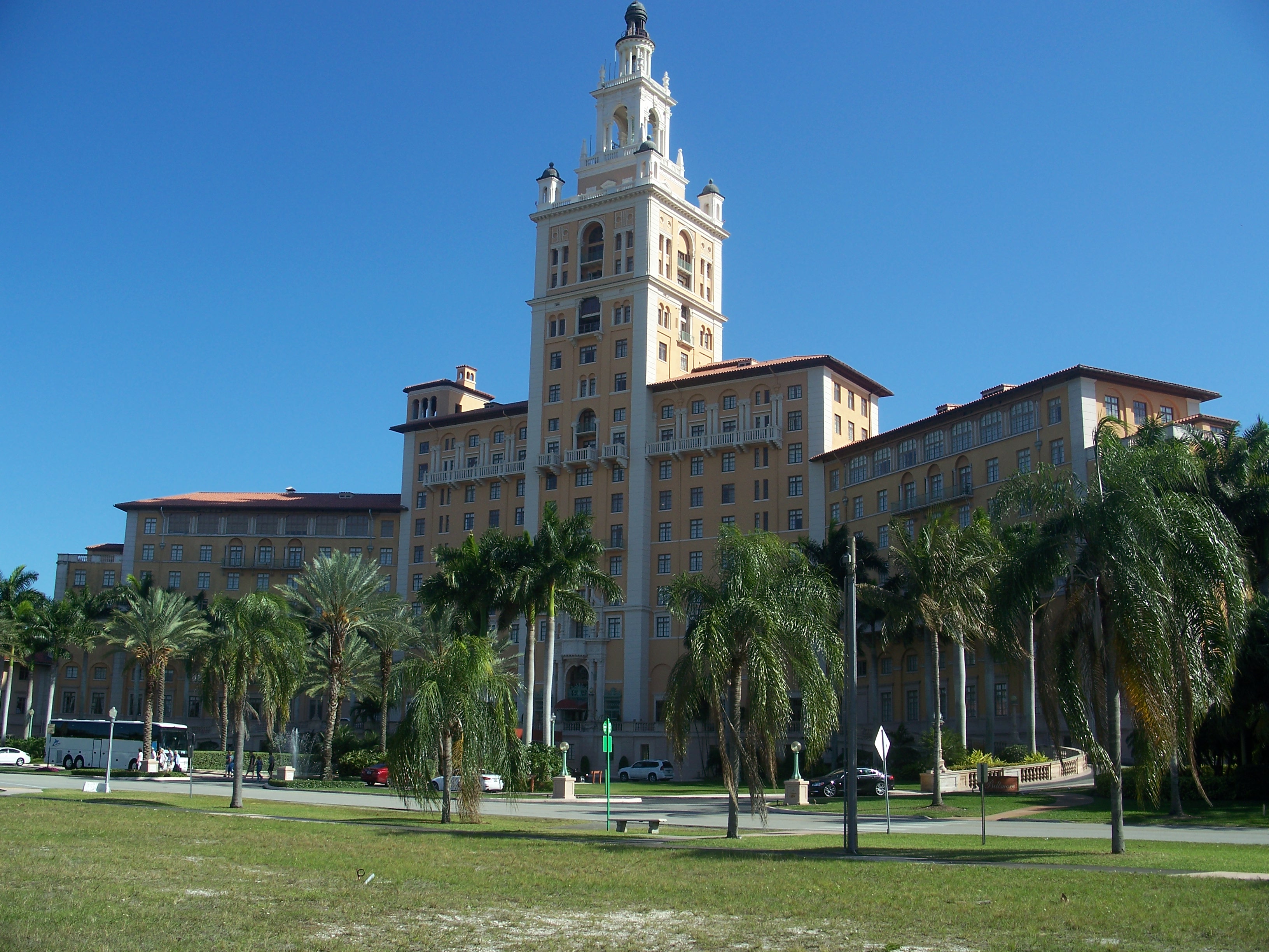 Mediterranean Revival hotel tower rising above palm trees and a green lawn.