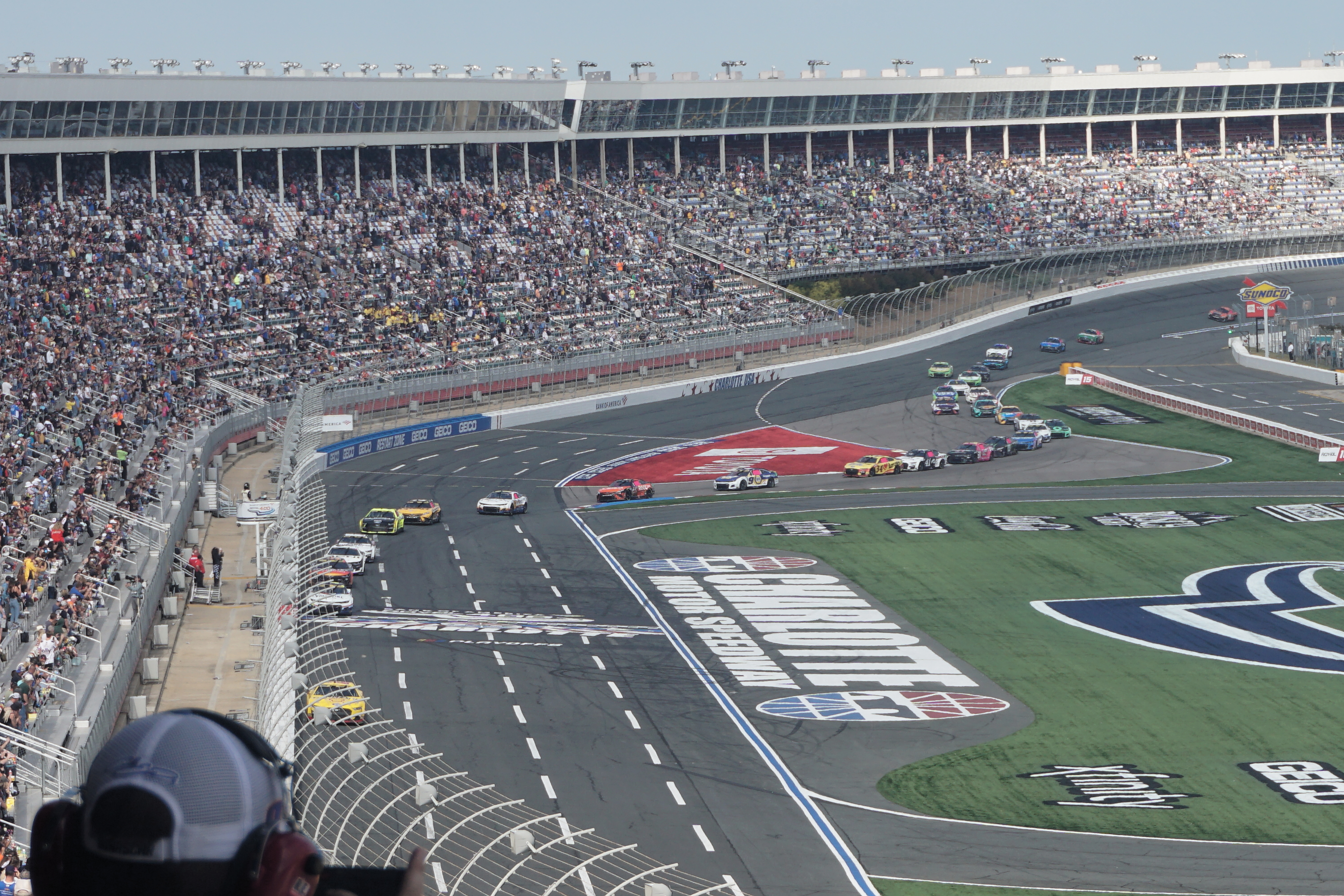 NASCAR stock cars racing on an oval track with packed grandstands in the background.