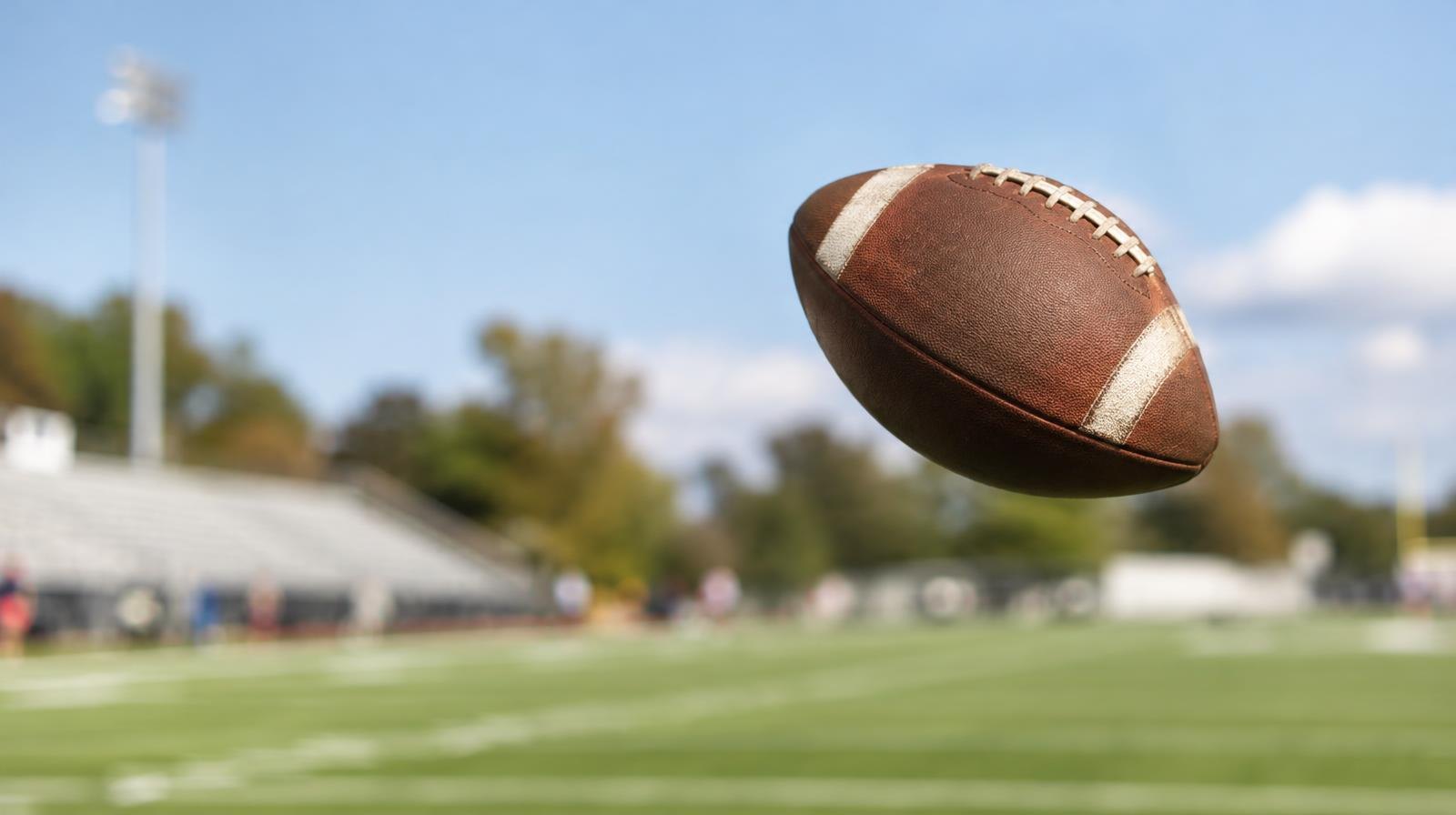 A football spiraling through the air above a green grass field.