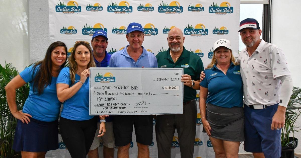 Group of seven people holding a large ceremonial check in front of a branded backdrop.