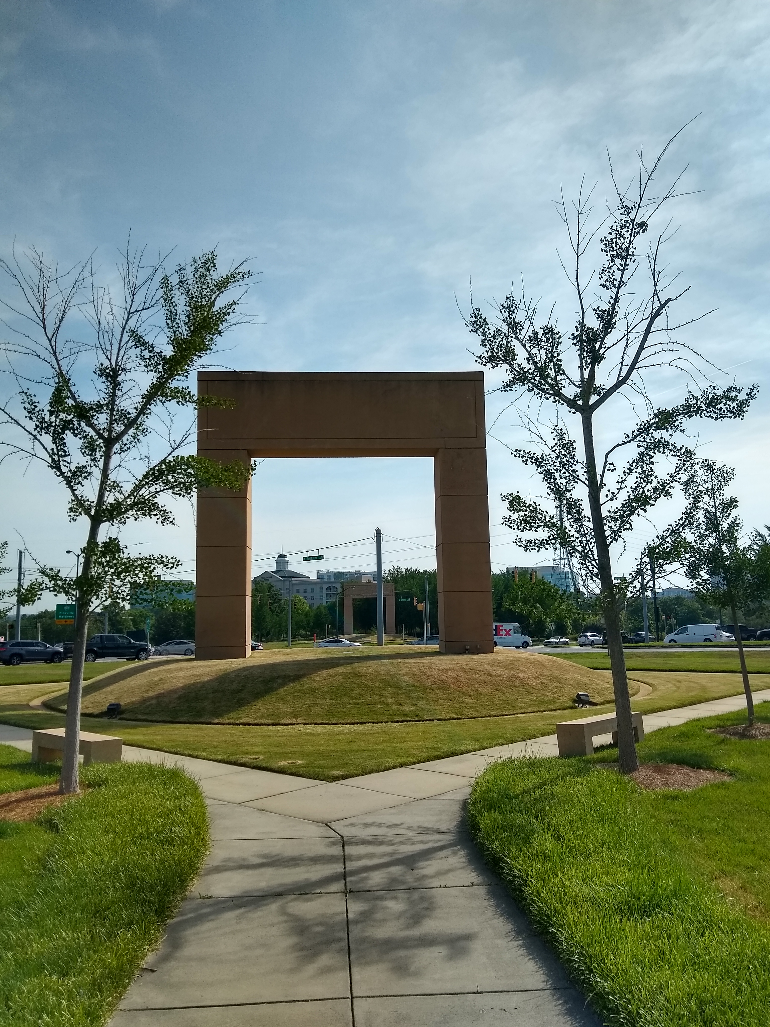 Large rectangular stone arch on a grassy mound with a pedestrian path leading toward it.
