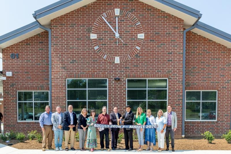 Group of adults holding a banner in front of a brick school building with a large clock.