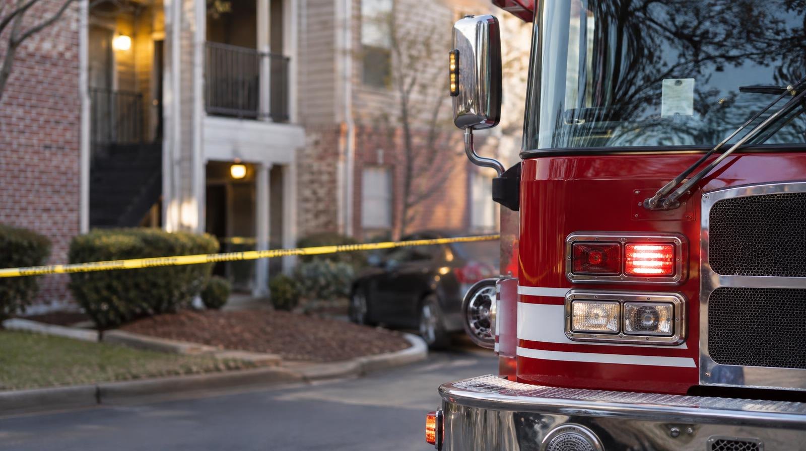A red fire engine parked beside an apartment building with yellow police tape.