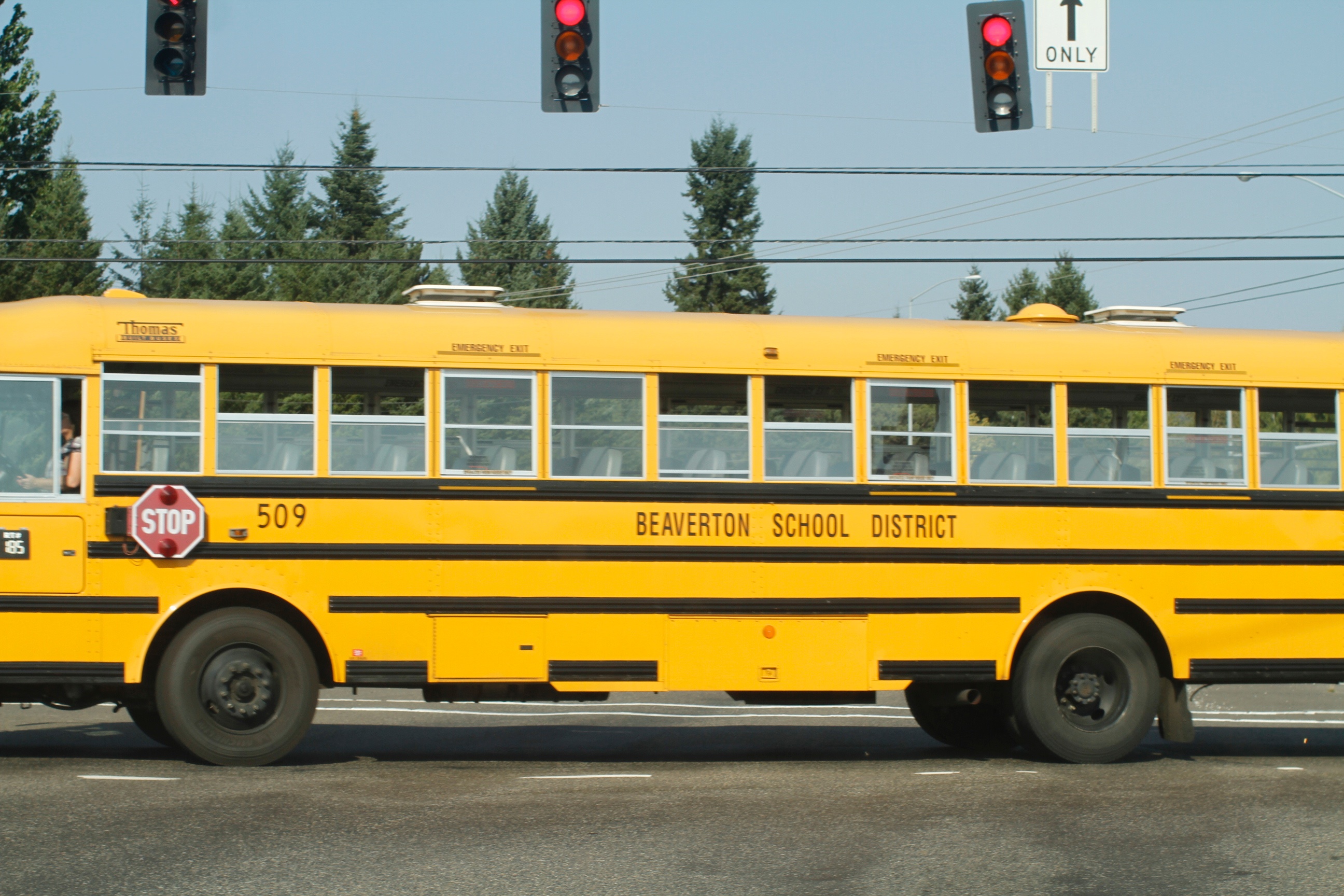 Yellow school bus labeled Beaverton School District stopped at a red traffic light.