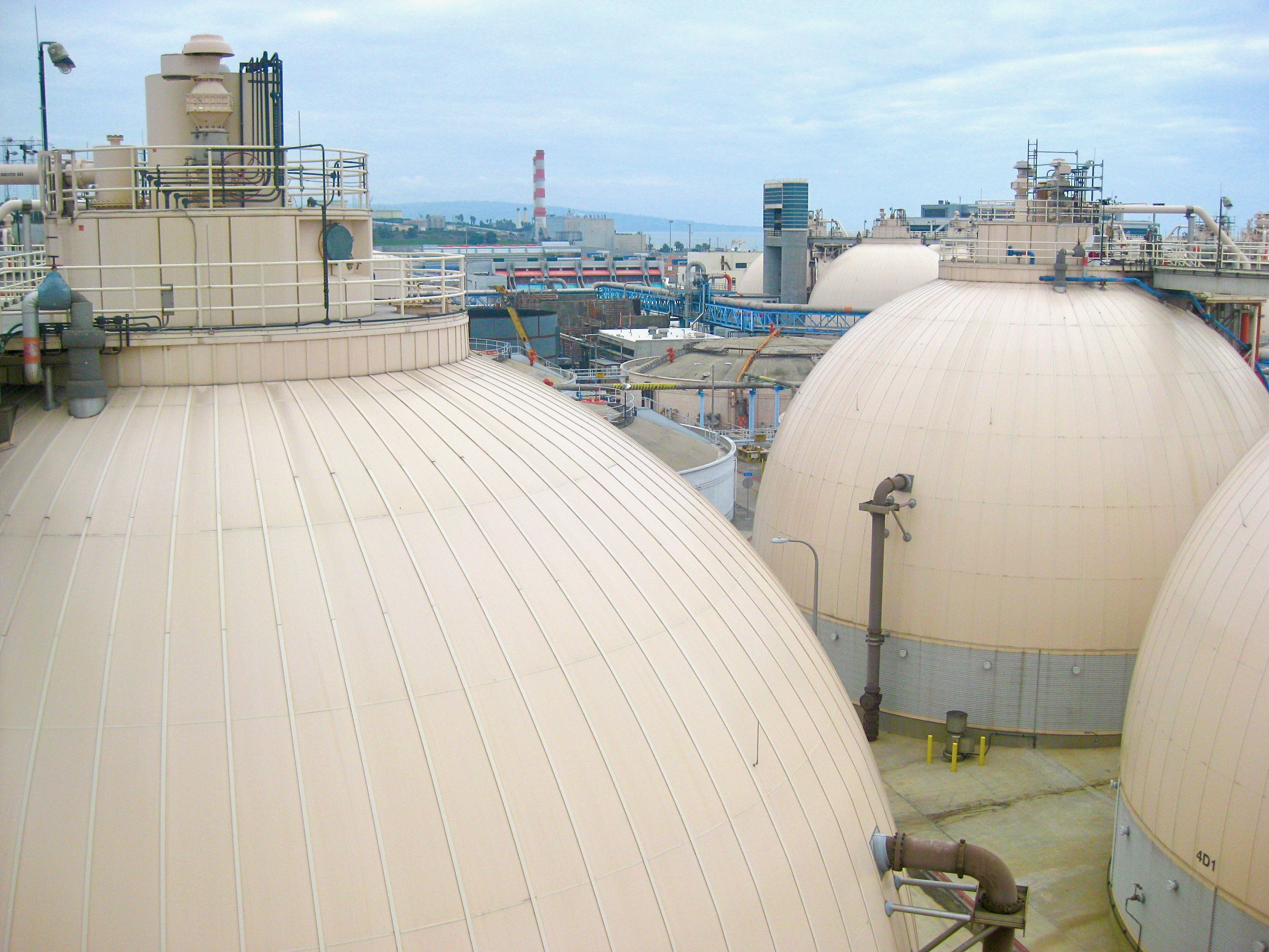 Dome-shaped digester tanks at a wastewater treatment facility near a body of water.
