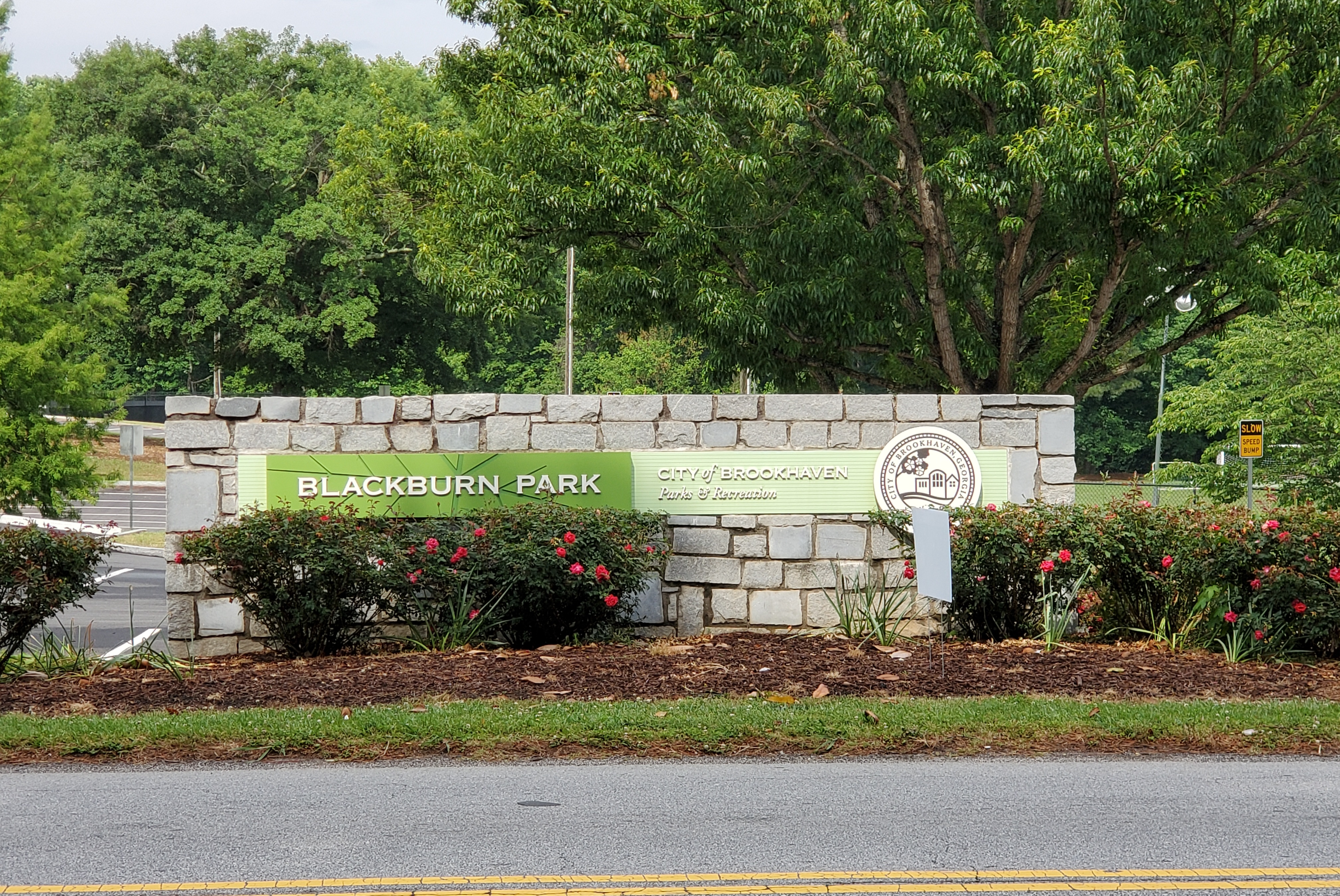 Stone entrance sign reading Blackburn Park with red flowering shrubs and a parks sign.