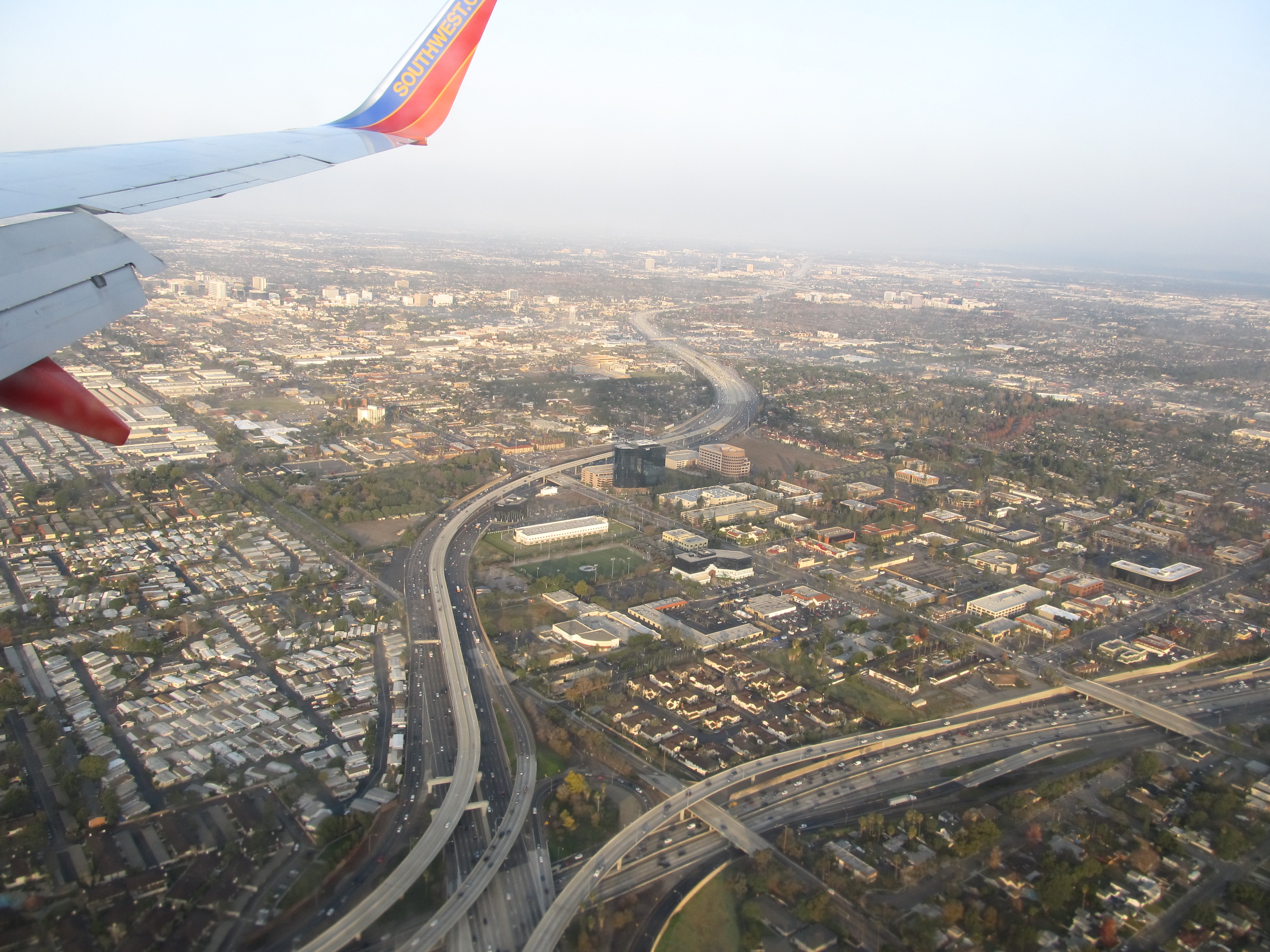 Aerial view of a dense urban grid of streets and freeways in Orange County, seen from an aircraft window.