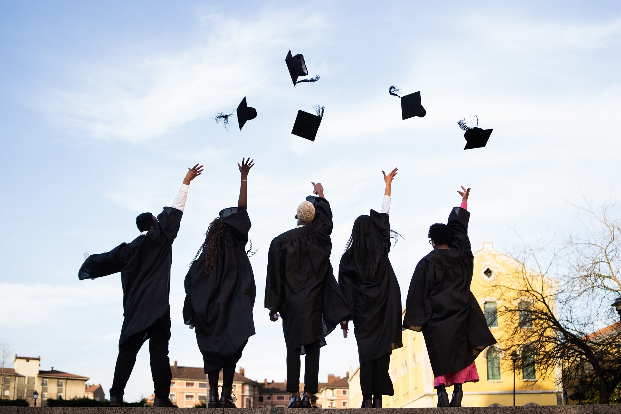 Graduates wearing black robes throwing mortarboards skyward, radiating excitement during commencement ceremony on bright outdoor setting
