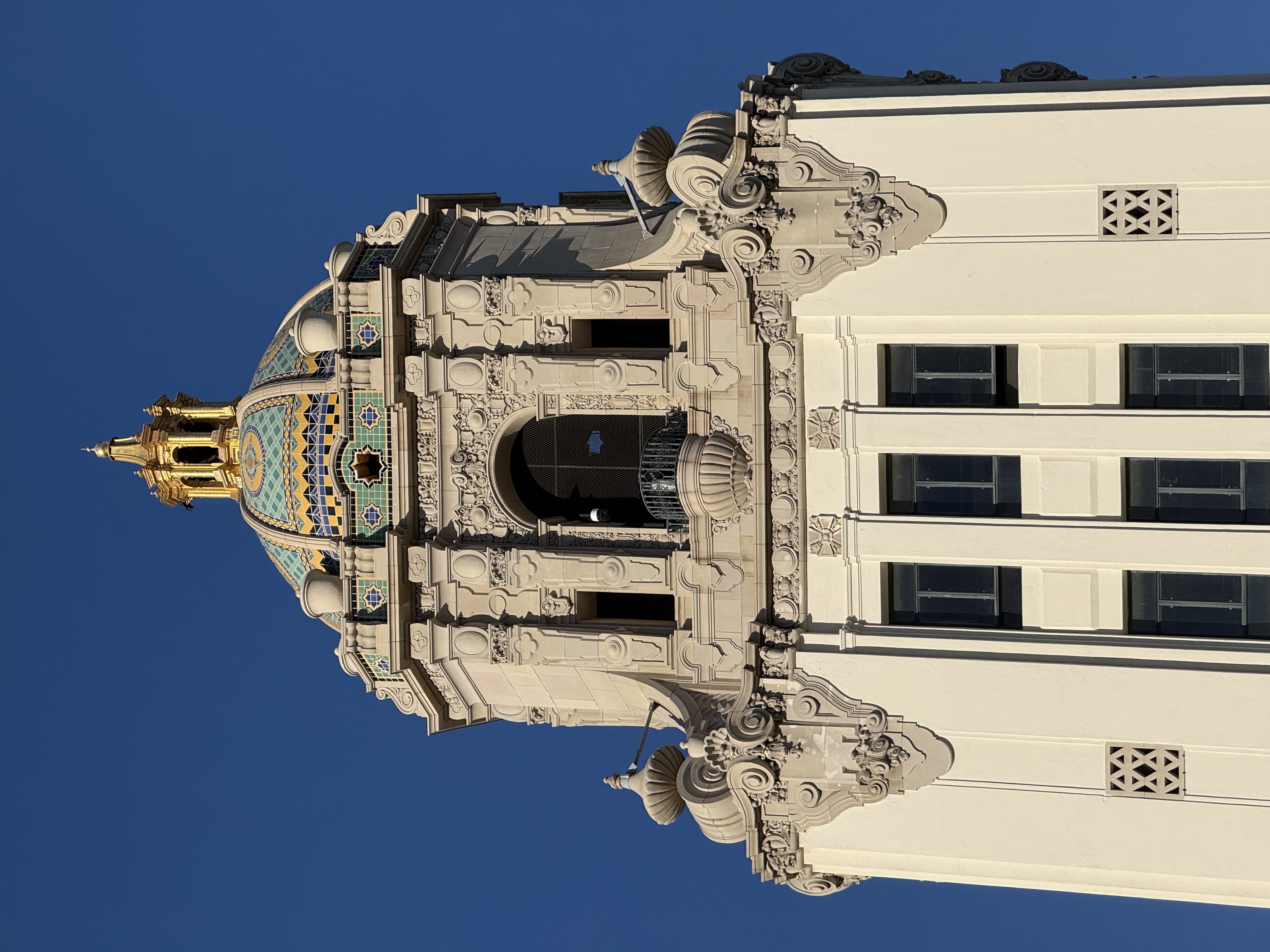 Ornate tiled dome and decorative tower of a government building against blue sky.