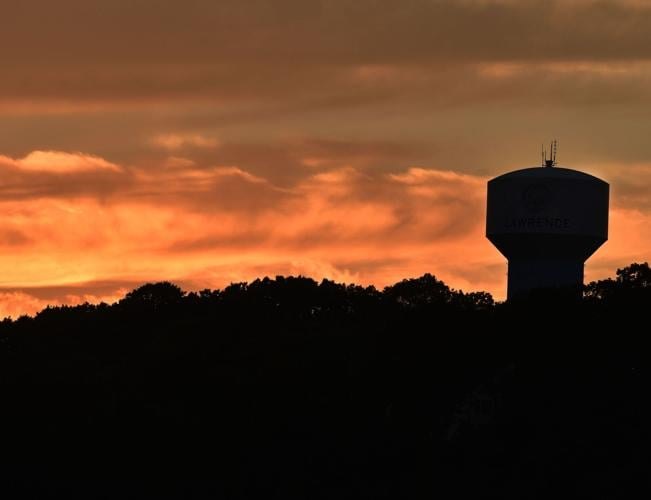Orange sunset behind silhouetted treeline and water tower under smoke-filled skies.