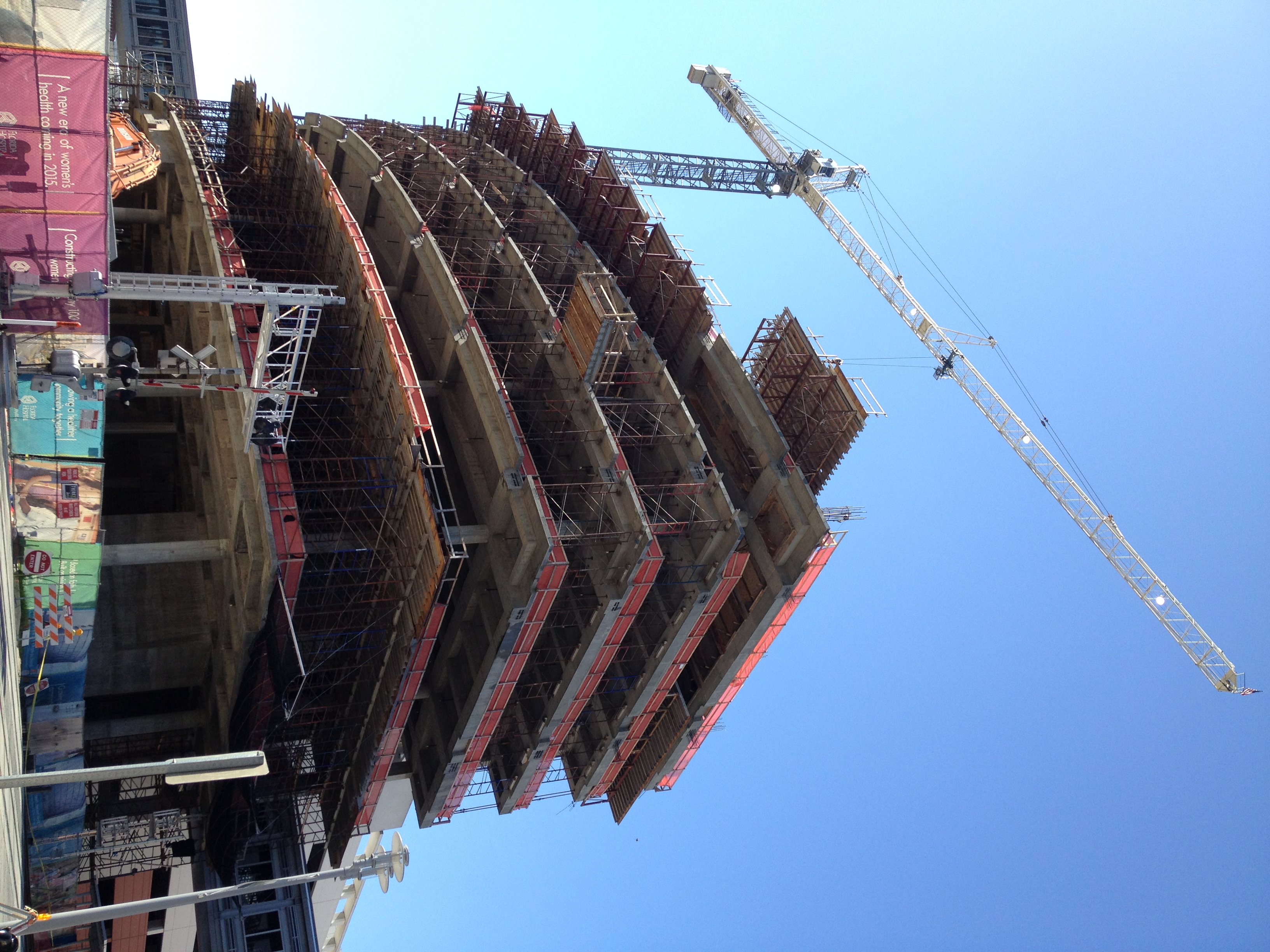 A multi-story building under construction with scaffolding and a tall tower crane against a clear blue sky.