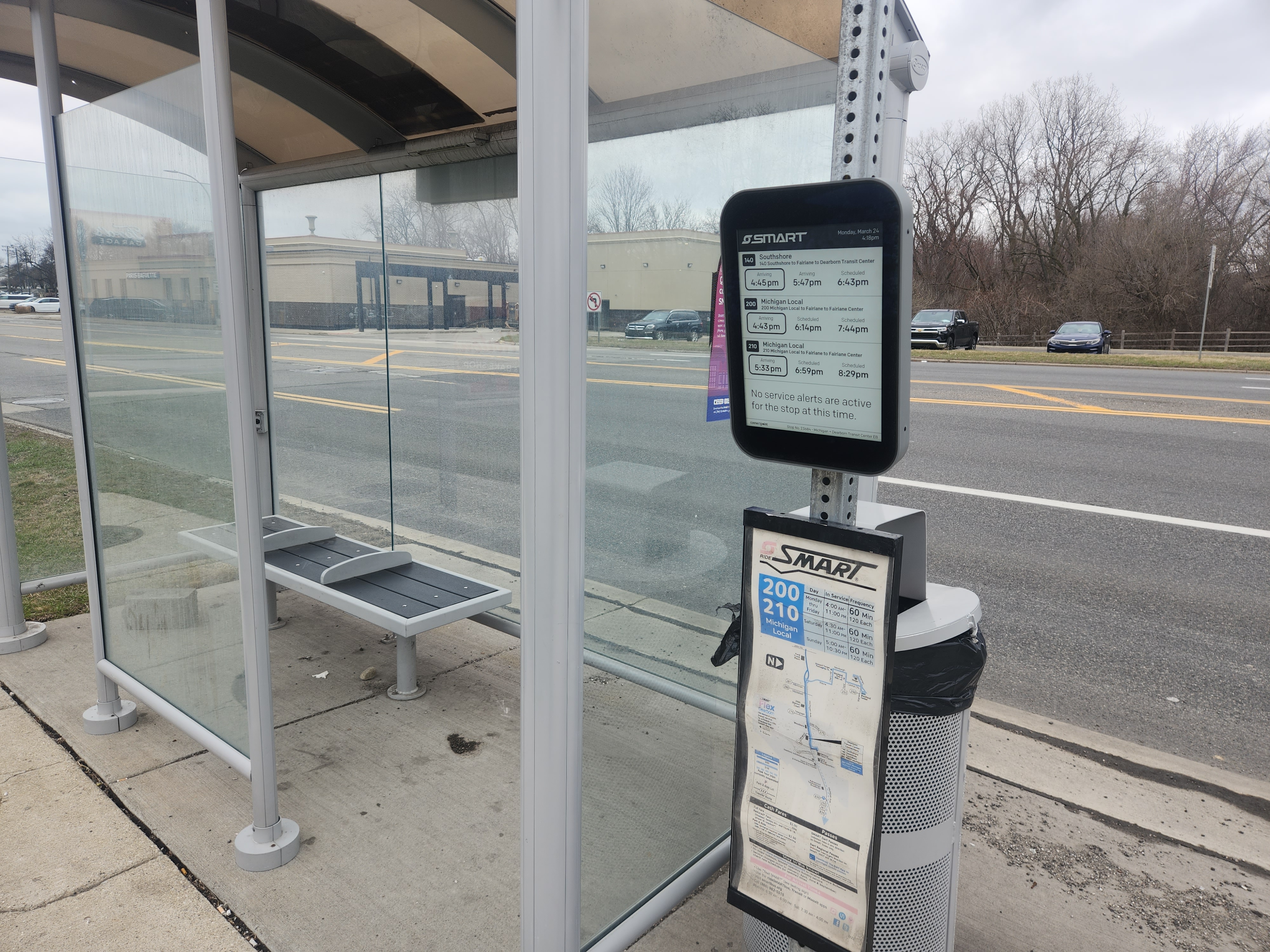 Glass-paneled SMART bus shelter with digital display and bench along a suburban road.