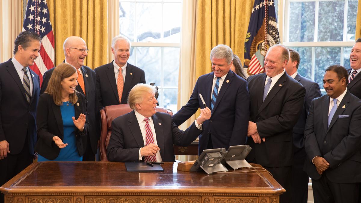 Officials gathered around a desk in the Oval Office during a bill-signing ceremony.
