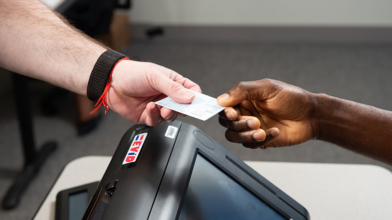 A voter presents an identification card to an elections poll worker at a check-in station.