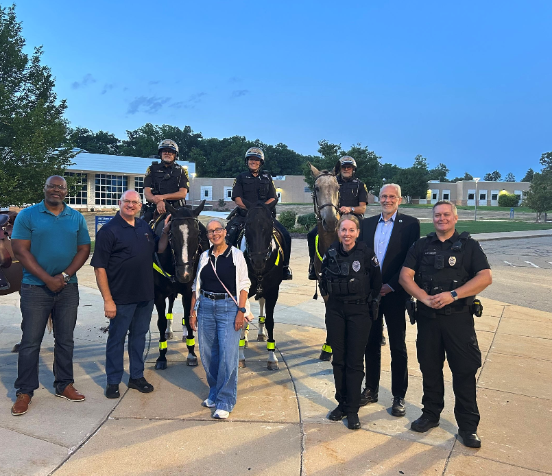 City officials stand with three East Lansing police officers on horseback outside a building ahead of MSU's Welcome Weekend.