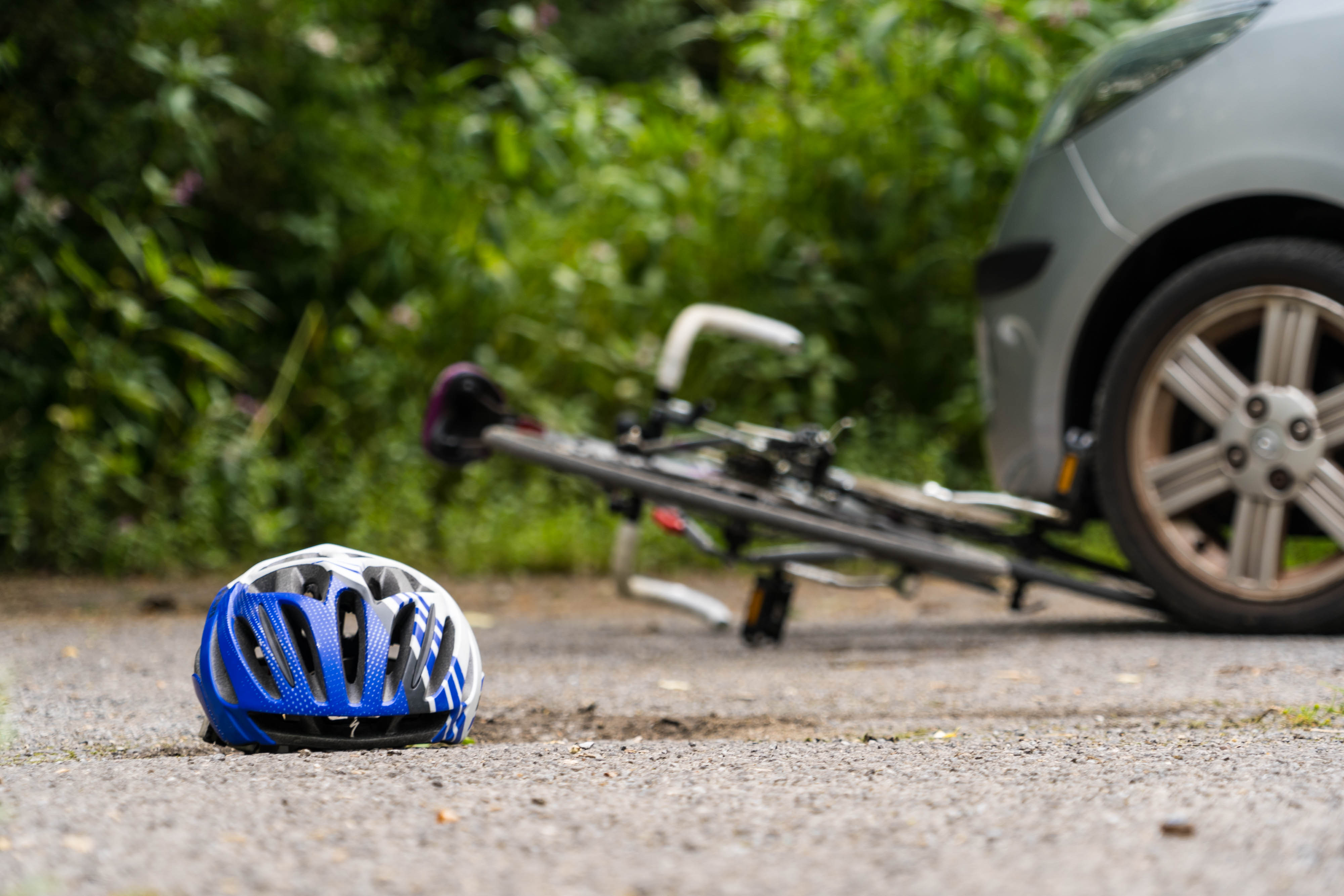 A bicycle helmet on pavement with a bicycle trapped under a car wheel behind it.