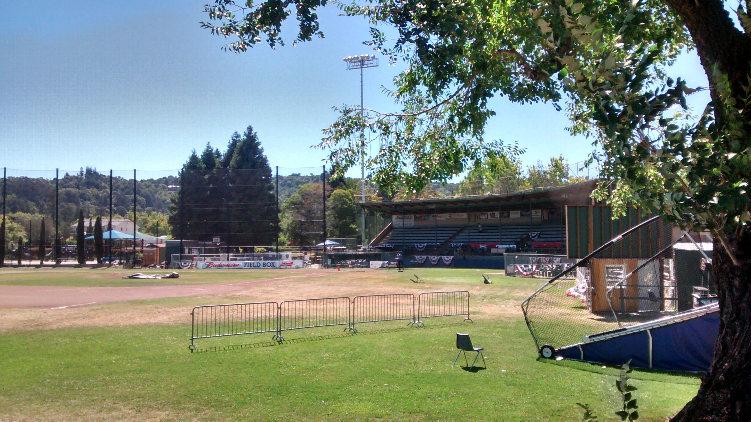 A baseball field with grandstand, fencing, and a light tower at a sunny city park.