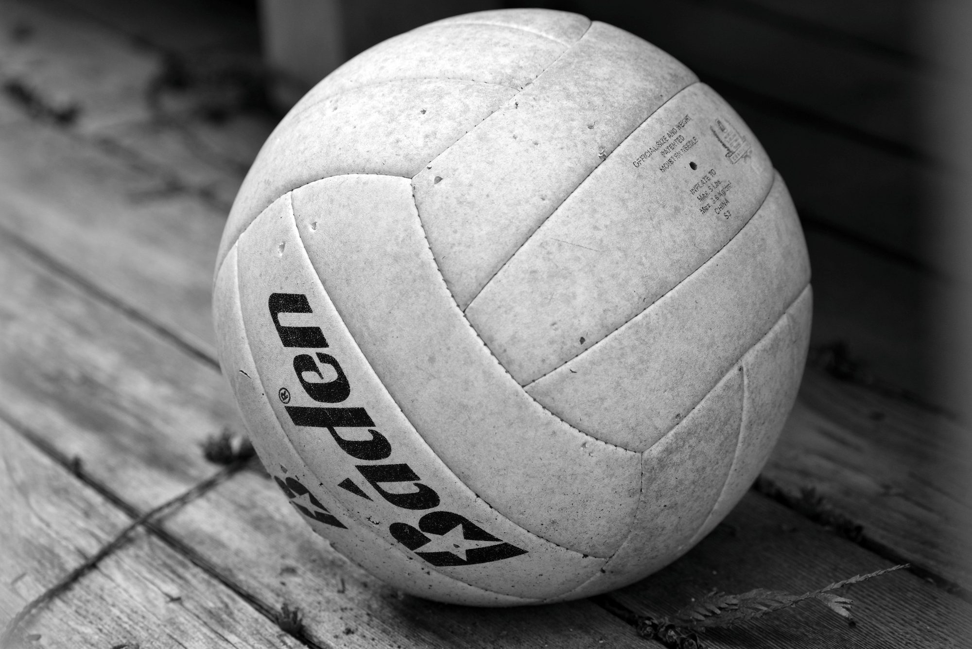 Close-up black and white photo of a volleyball resting on a wooden surface.
