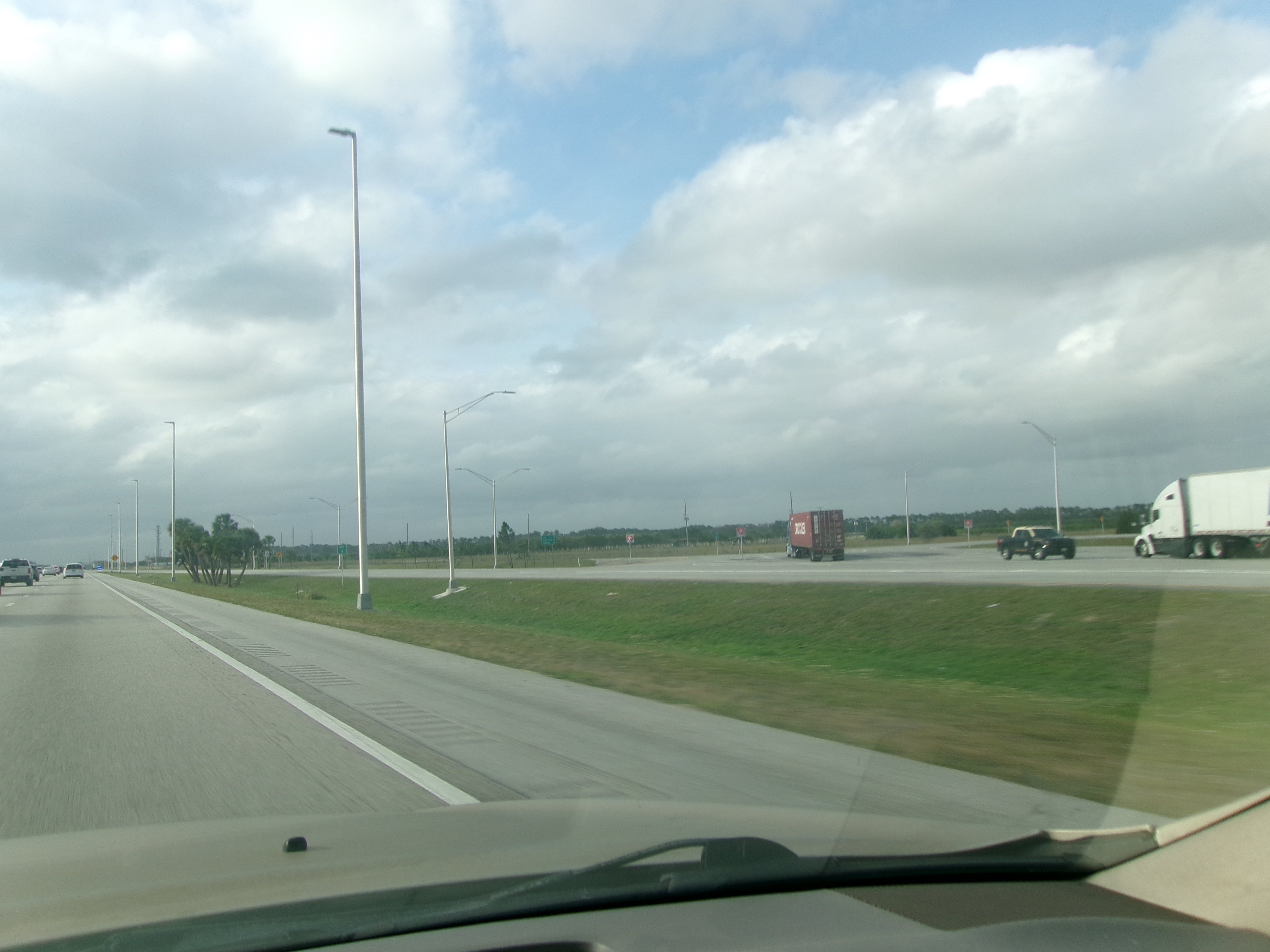 Multi-lane interstate highway with trucks and light poles visible from inside a vehicle.