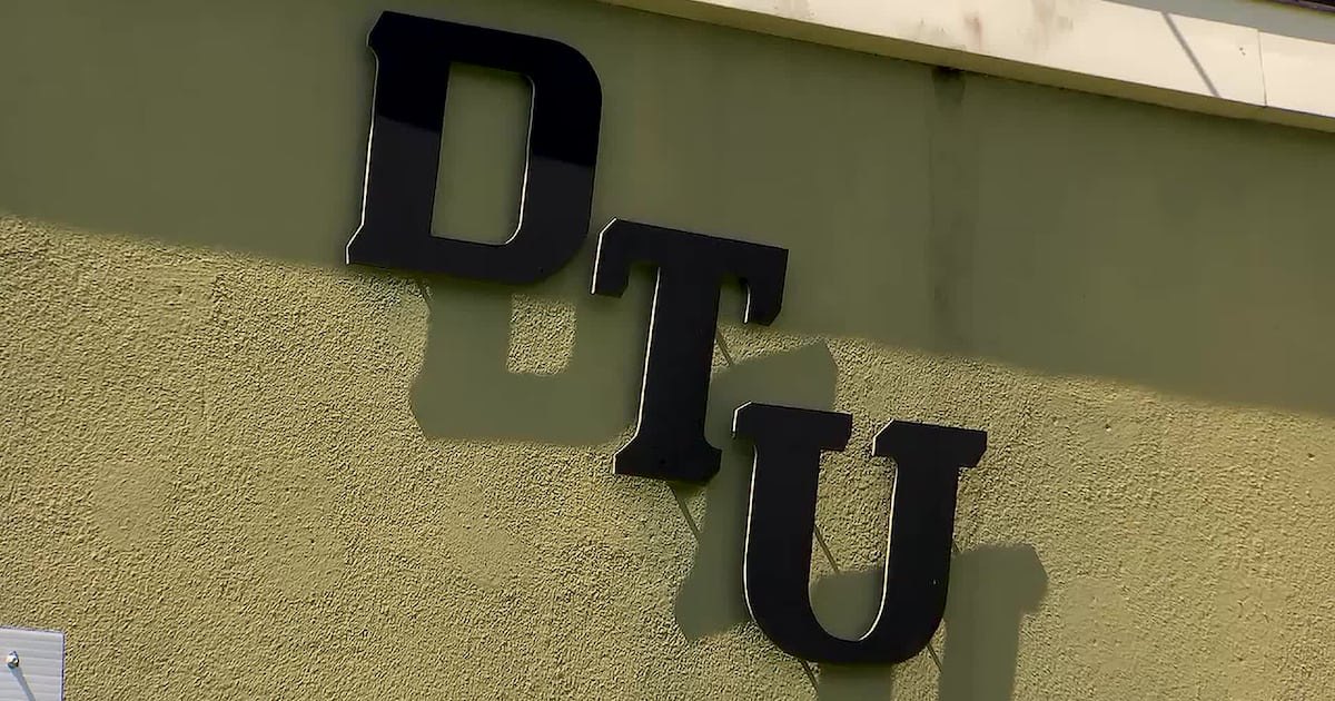 Black raised letters spelling DTU mounted on a green stucco exterior wall.